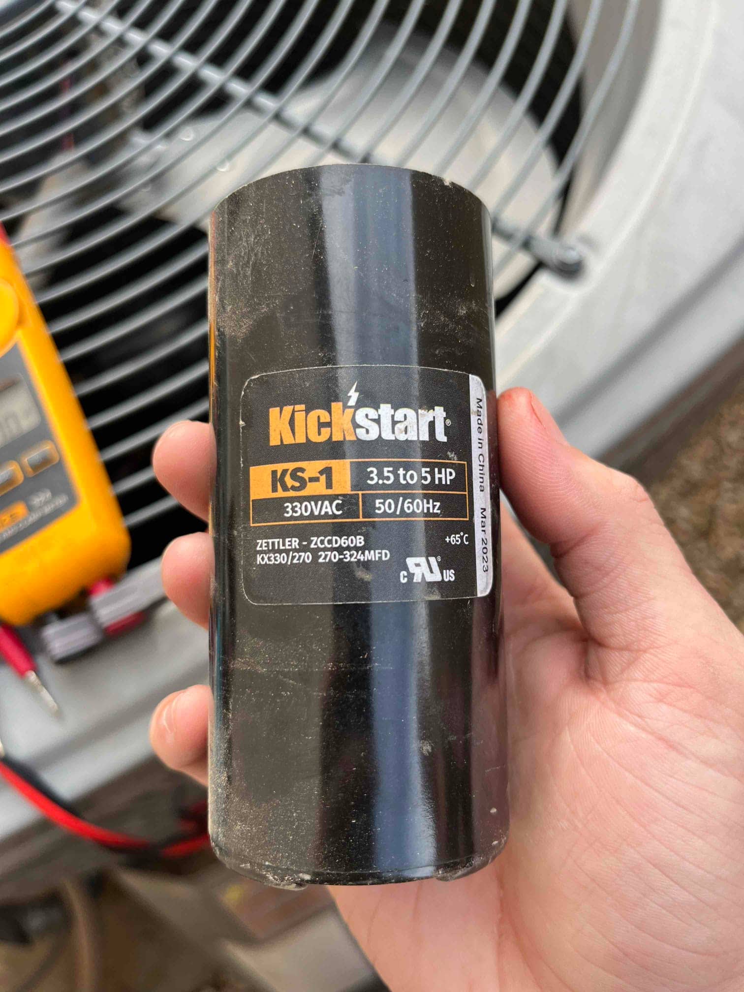 Start assist capacitor kit labeled KS-1, 330VAC, 3.5 to 5 HP, 50/60Hz, held near an outdoor condenser.