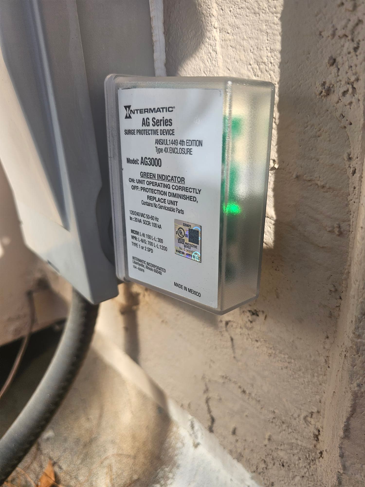 Surge protective device installed beside outdoor HVAC disconnect, green indicator light on showing operational status.