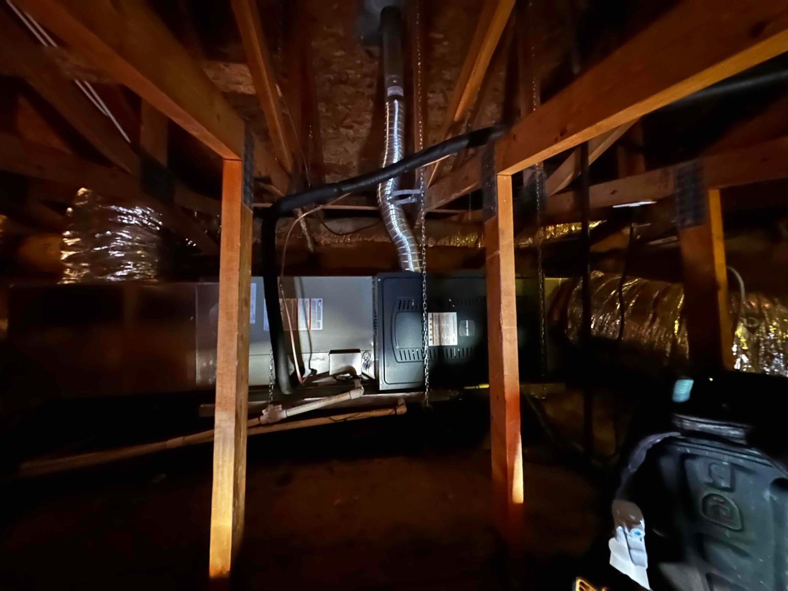 Suspended air handler installed in attic with insulated duct connections, drain piping, and support chains visible between joists.