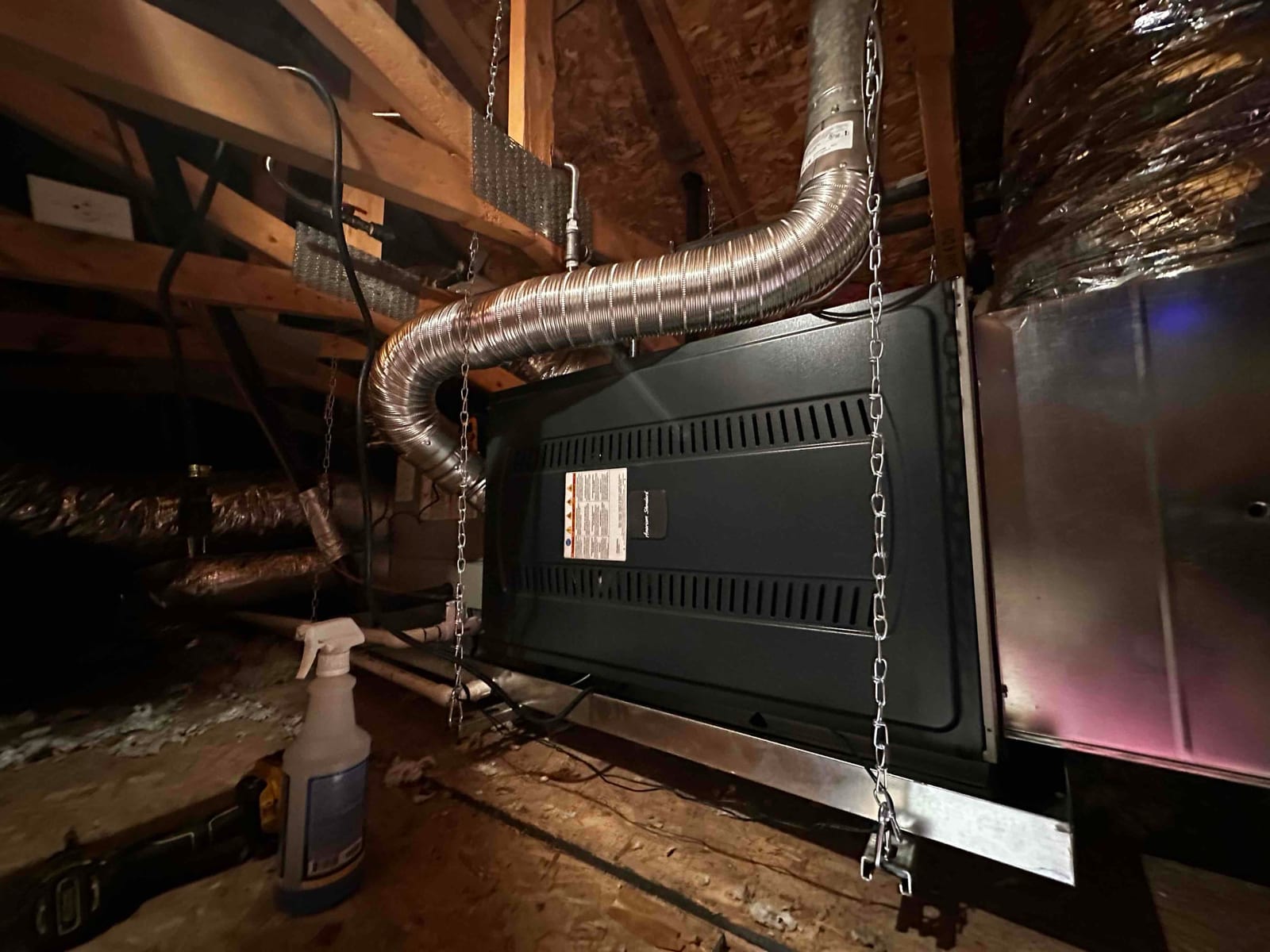Suspended attic air handler with metal drain pan, flex duct connections, and hanging chains installed and supported from roof framing.