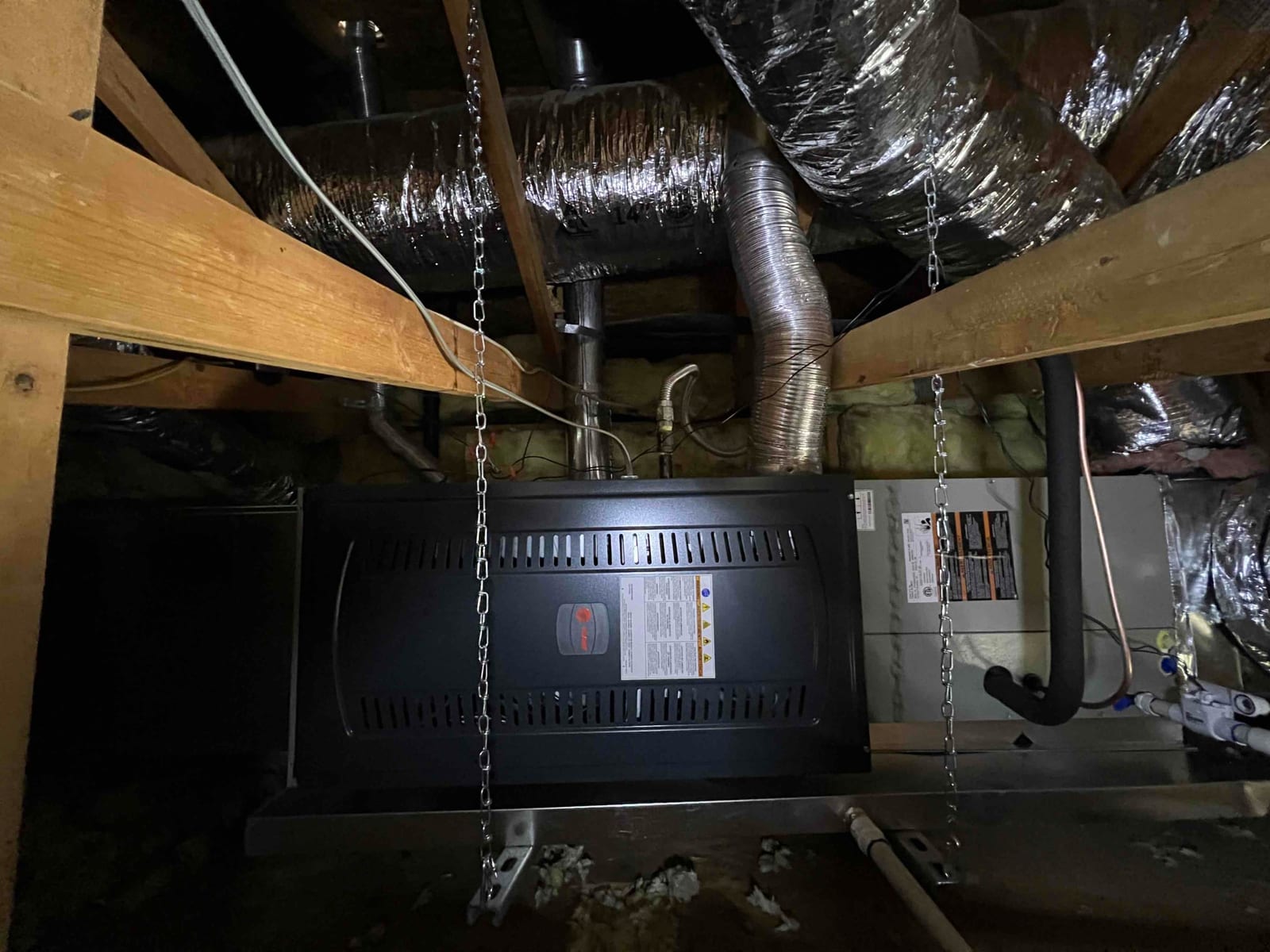Suspended gas furnace and evaporator coil assembly installed in attic with insulated ductwork, condensate piping, and refrigerant line set connected.