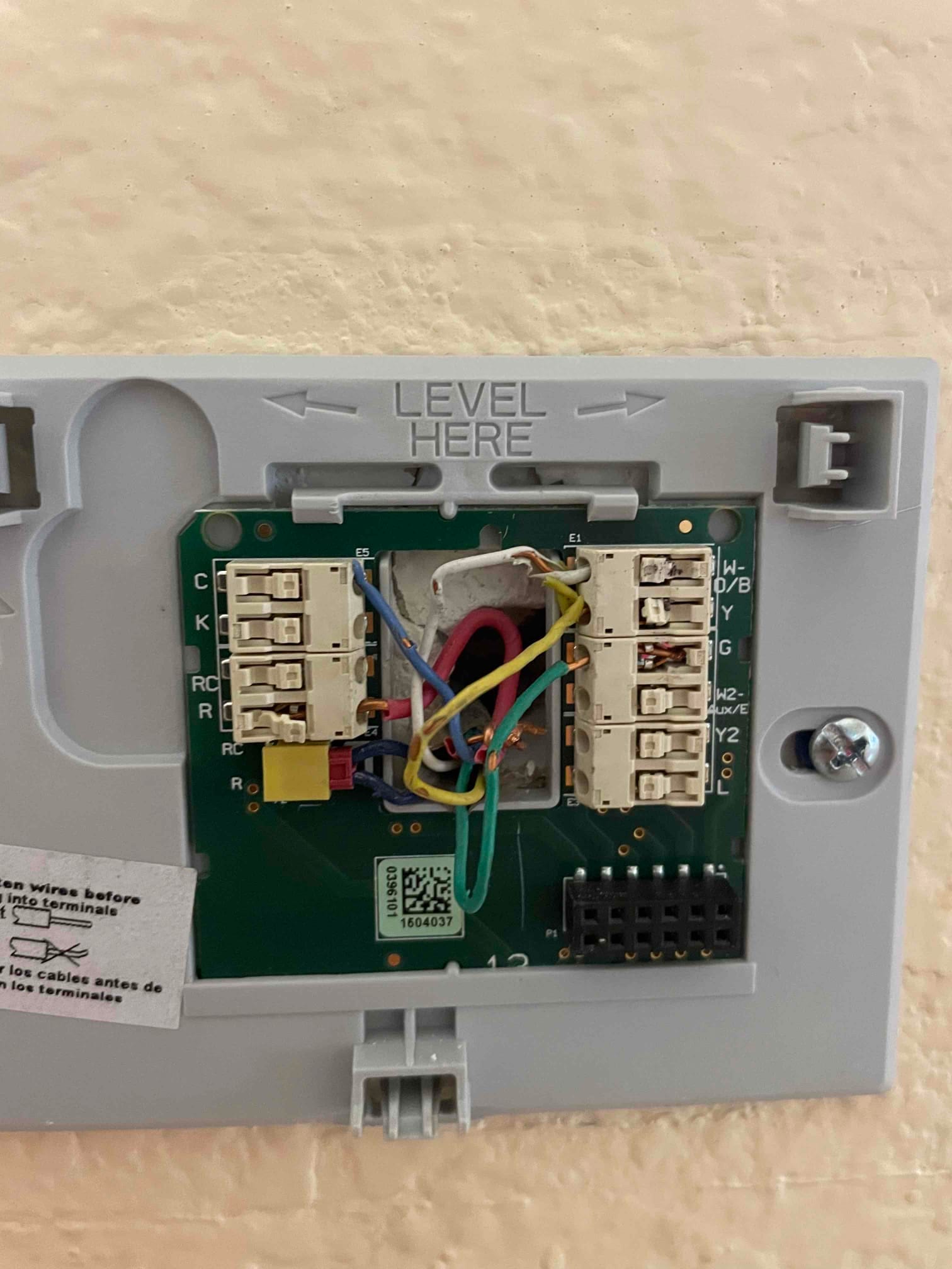 Thermostat backplate with multicolored control wires landed on labeled terminals, including R, C, Y, G, and W.