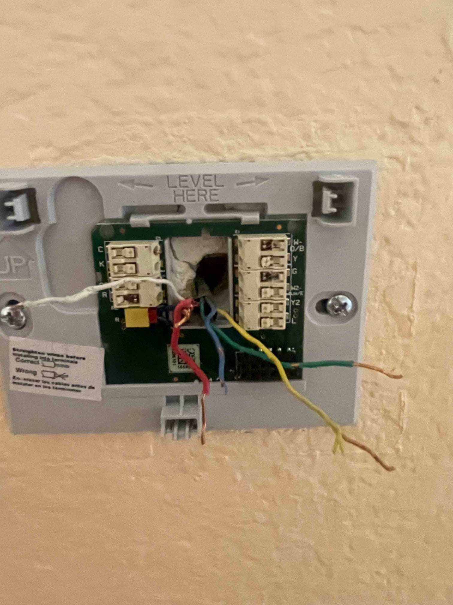Thermostat wall plate with exposed control wiring; several colored conductors disconnected and hanging beside labeled terminals.