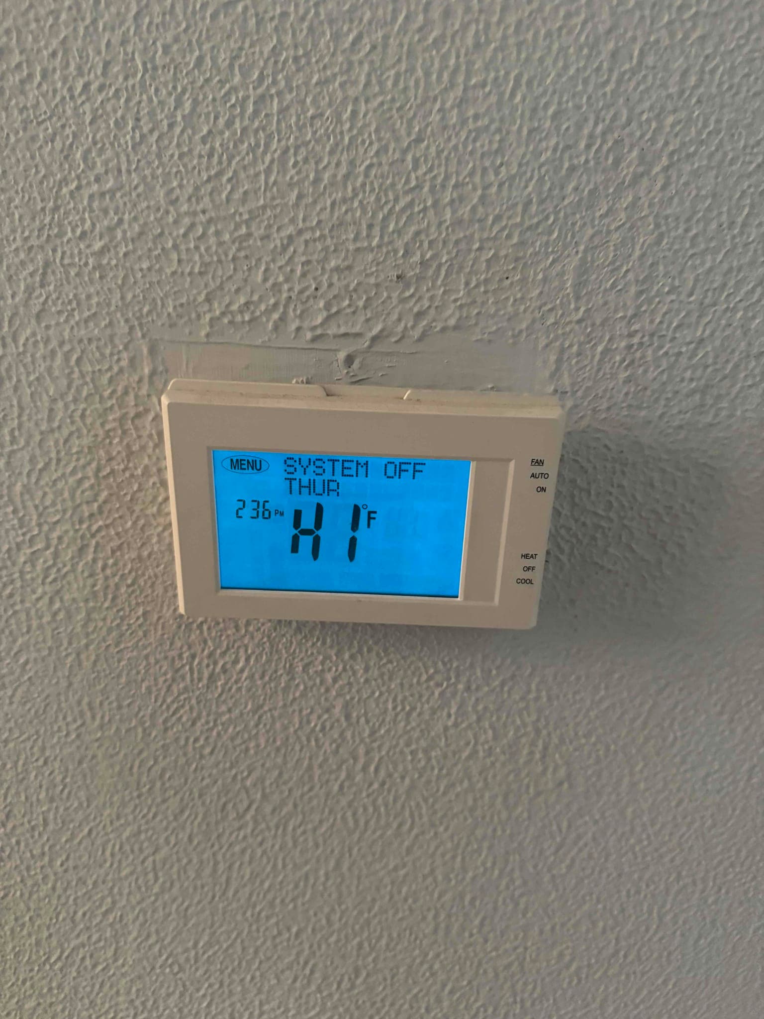 Wall-mounted digital thermostat displays system off and indoor temperature reading of 81°F on a blue backlit screen.