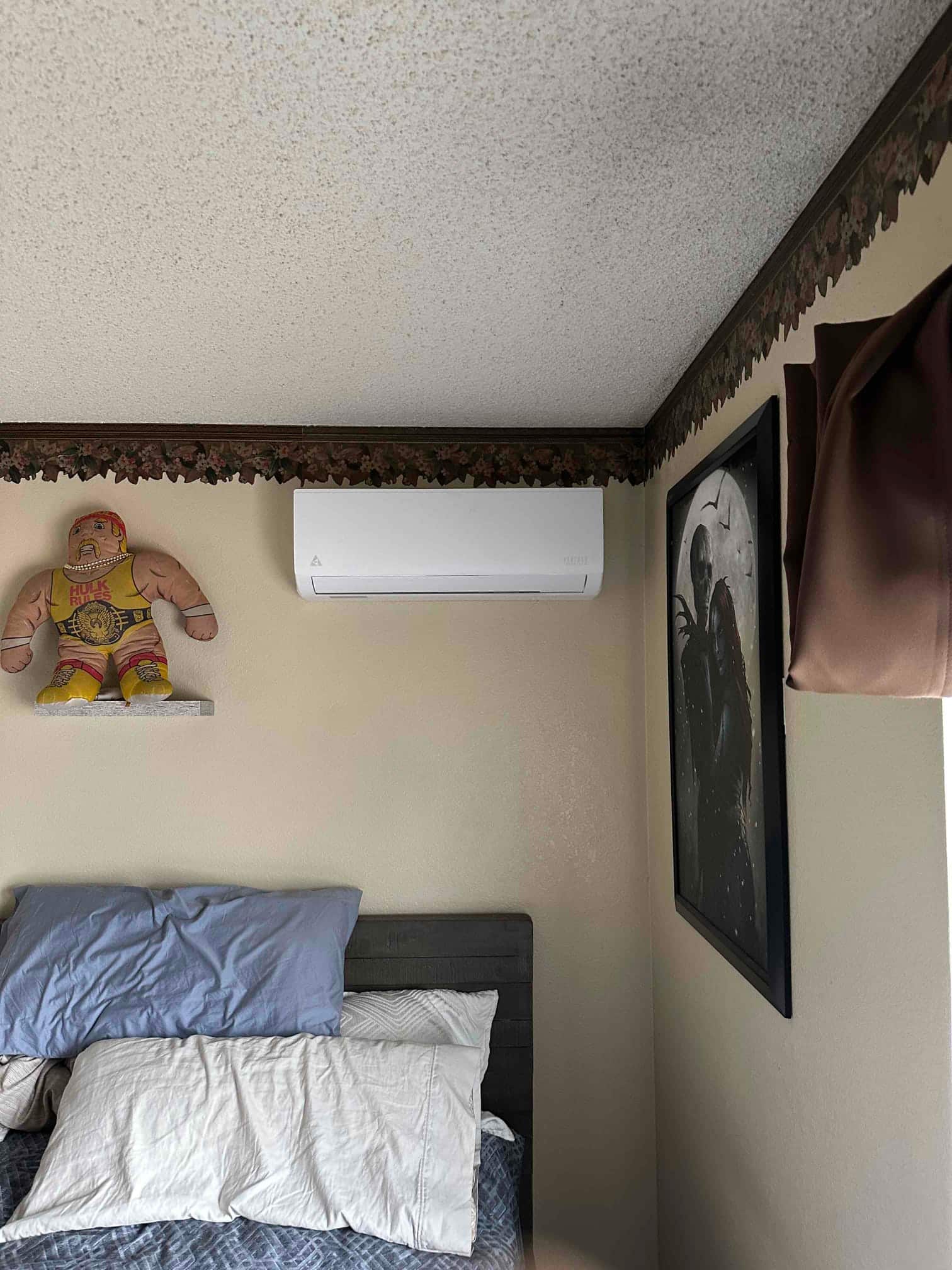 Wall-mounted ductless indoor unit installed above a bed, with clean wall penetration and tidy placement in the room.