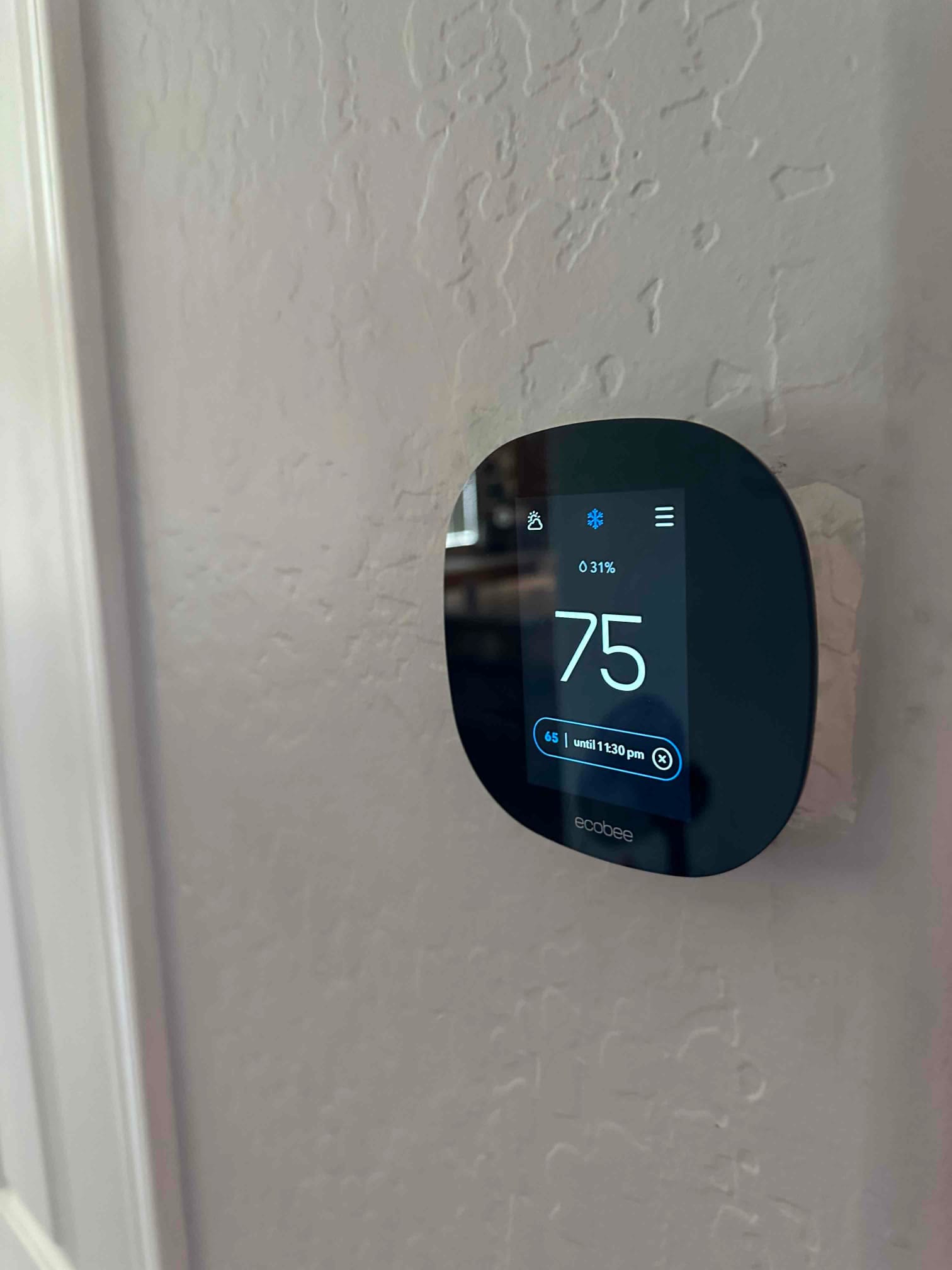 Wall-mounted smart thermostat displays 75 degrees and cooling mode after the new HVAC system installation.