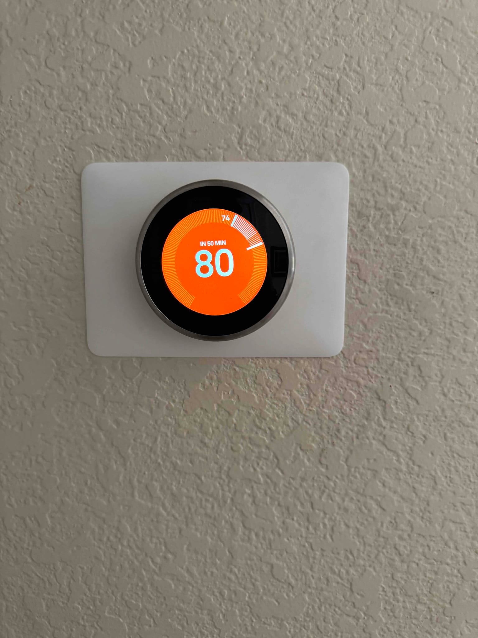 Wall-mounted smart thermostat installed on a trim plate, display showing 80 degrees and countdown for temperature change.