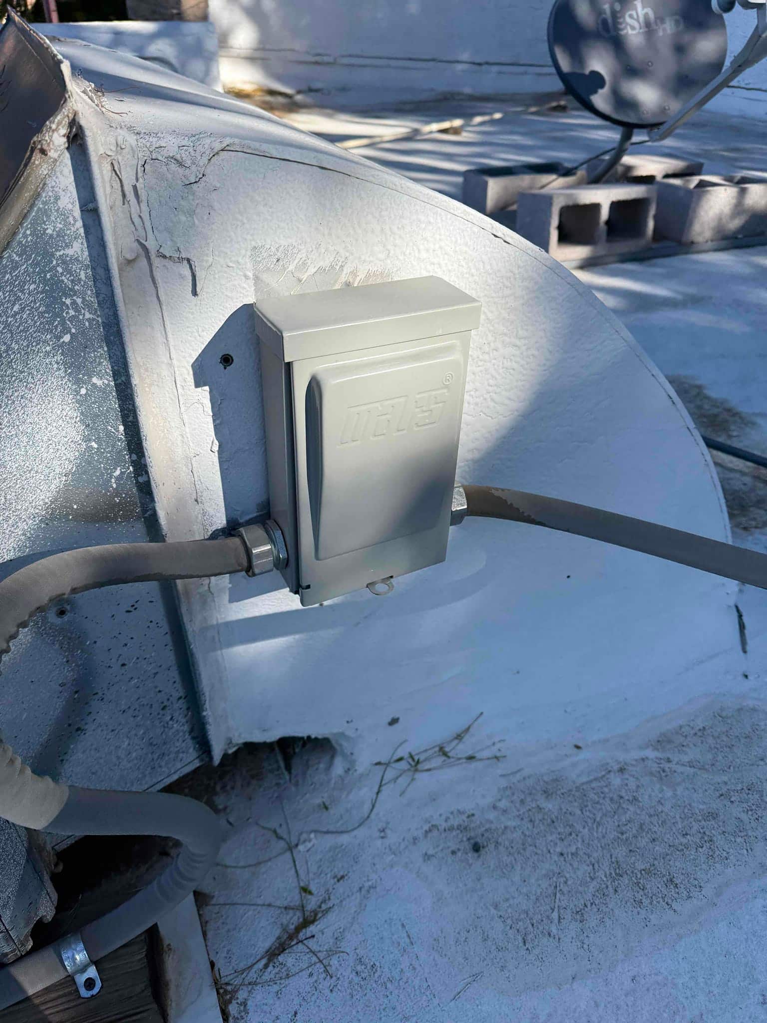 Weatherproof electrical disconnect box mounted on rooftop near HVAC ductwork with conduit entering from both sides.