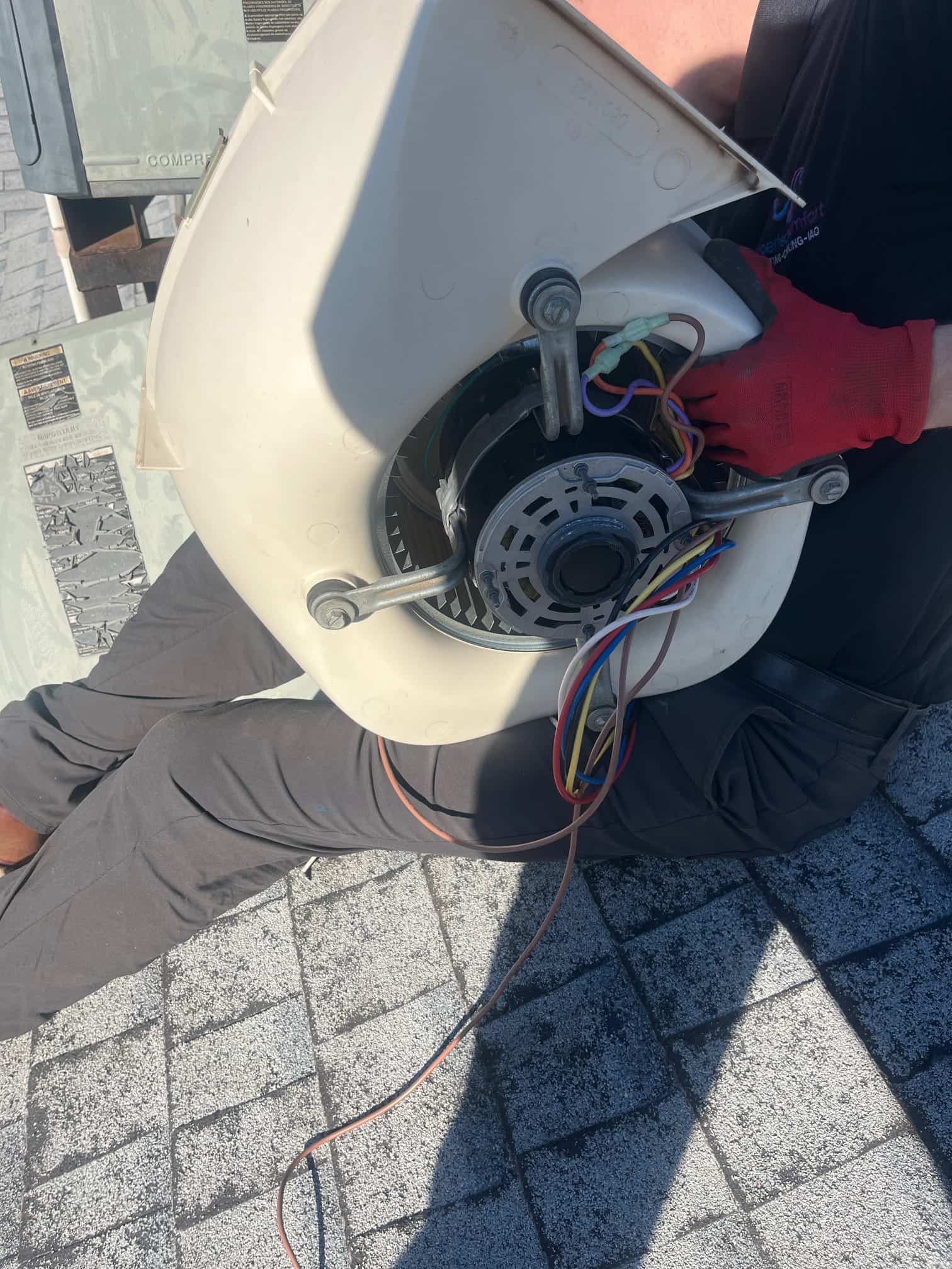 Blower housing with electric motor and multicolor wiring is held by a technician wearing a red glove during service.