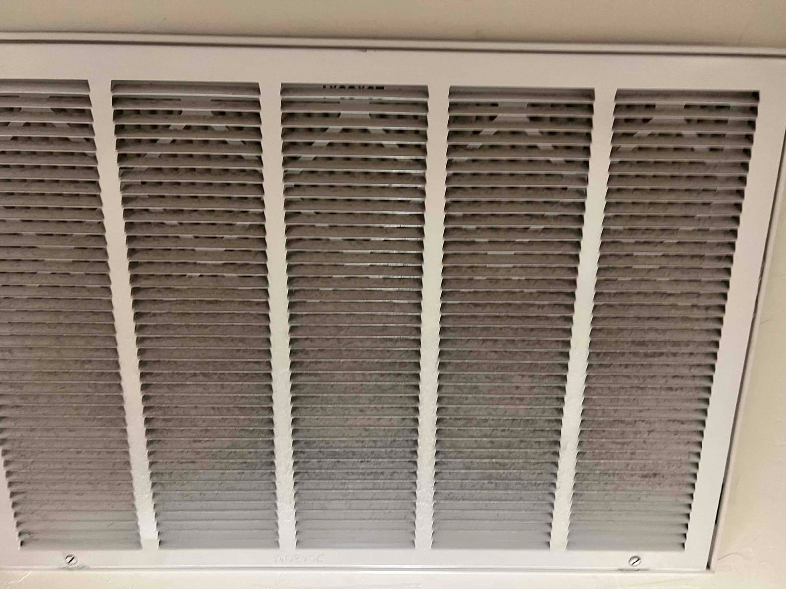 Ceiling return air grille with louvered cover; pleated air filter behind the grille shows uniform gray dust buildup.