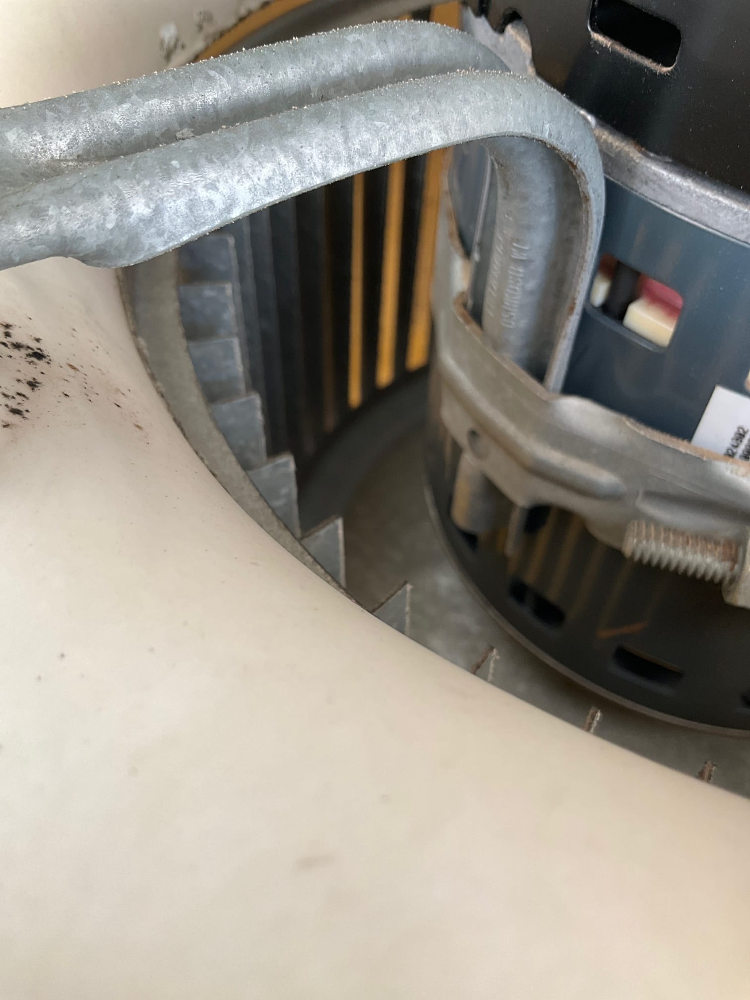 Close-up of blower motor and squirrel-cage fan wheel with metal mounting strap inside the air handler housing.