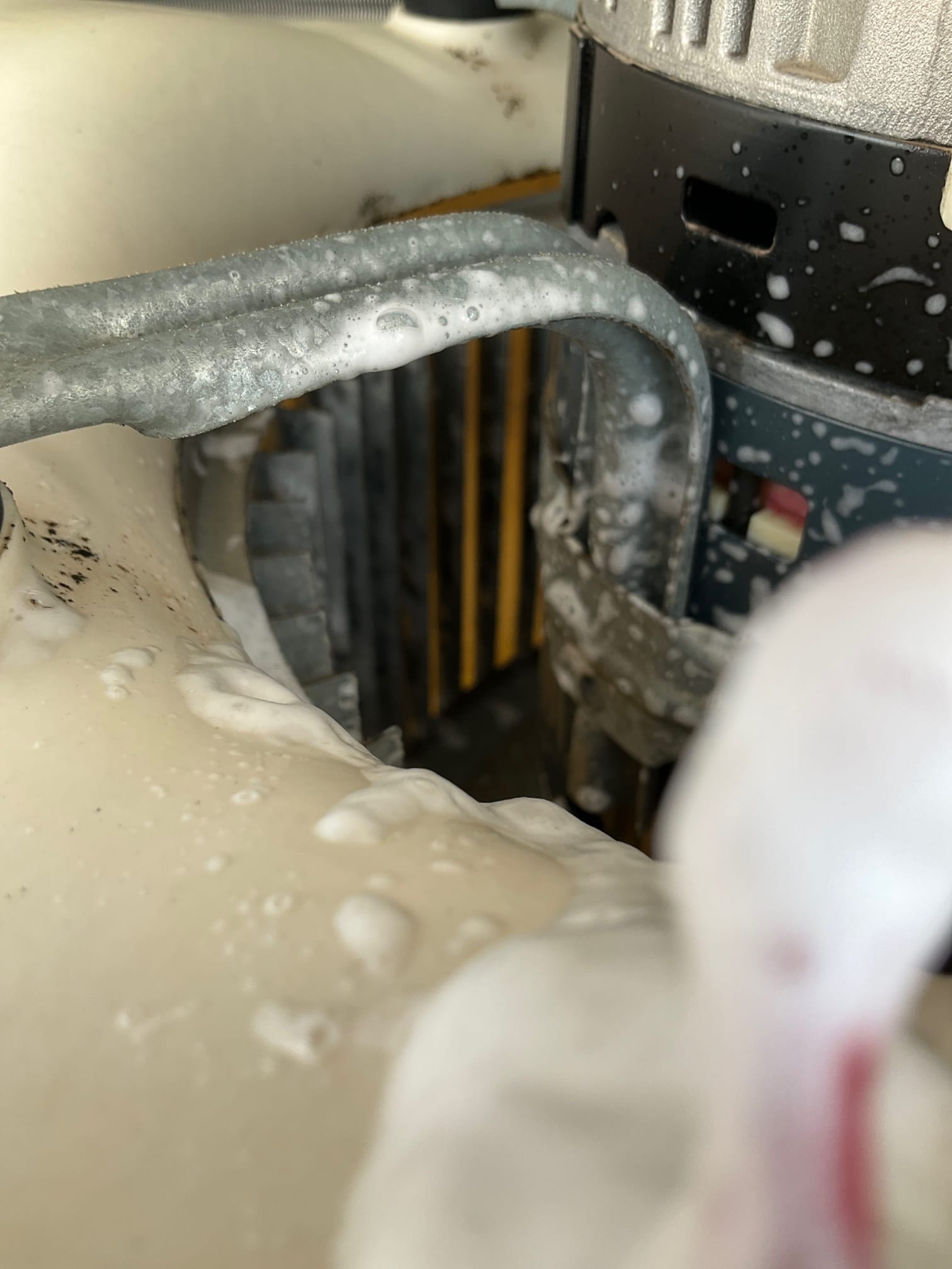 Close-up of condenser fan motor area with soap bubbles on metal tubing and shroud near the coil.