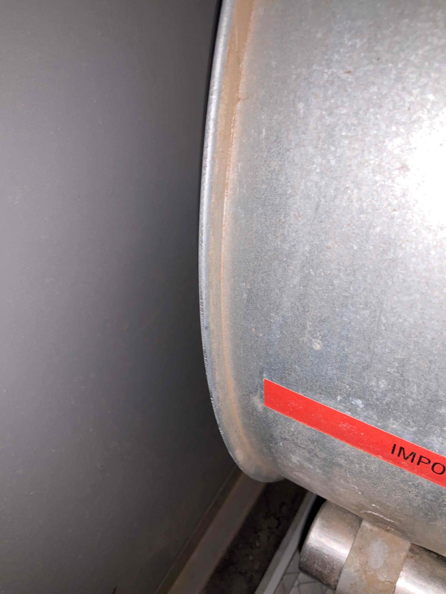 Close-up of a galvanized metal cylindrical housing with a red safety label on the side, showing light dust.