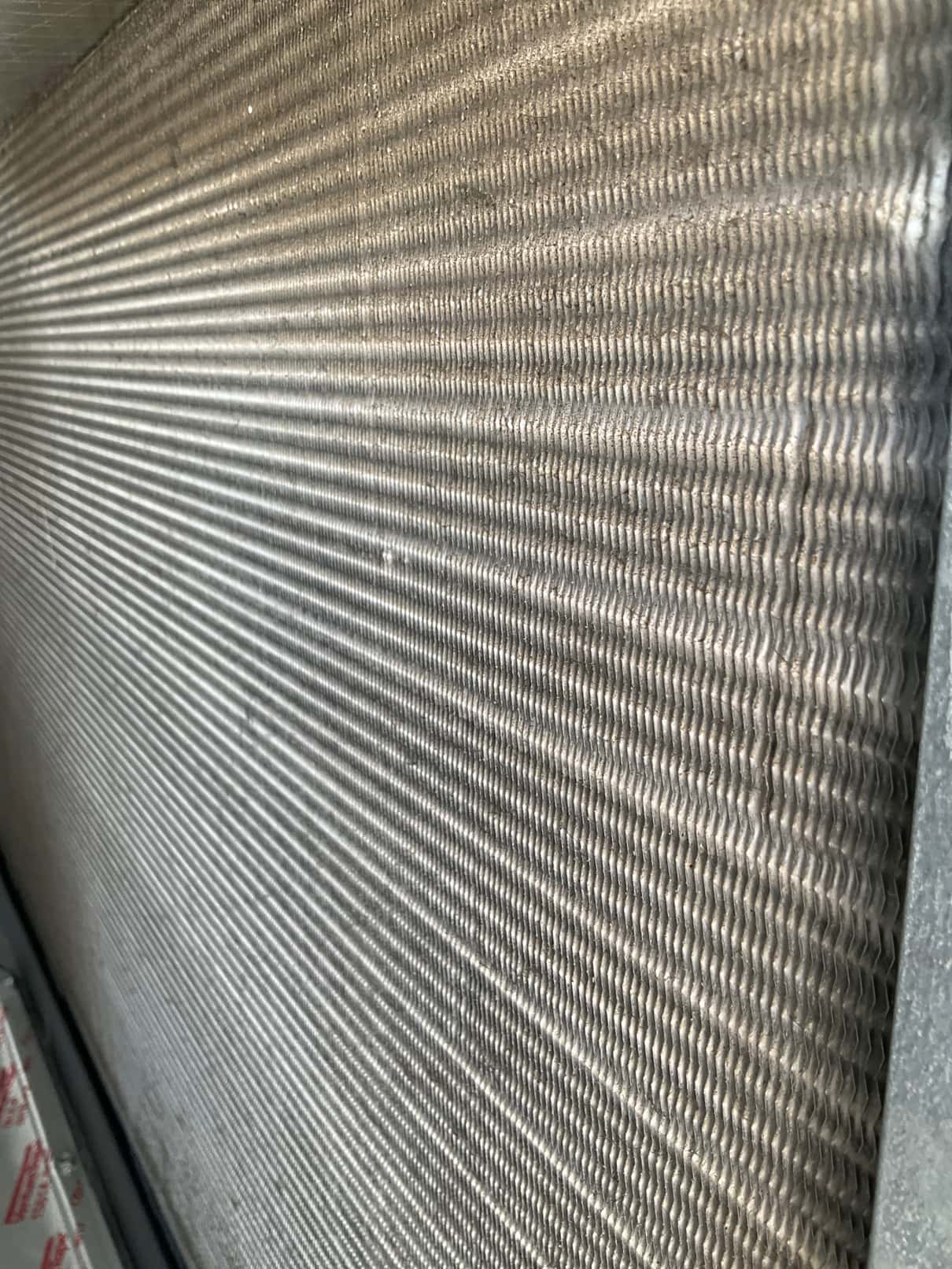 Close-up of HVAC condenser coil fins inside the unit, showing tightly spaced aluminum fins with light surface dust.