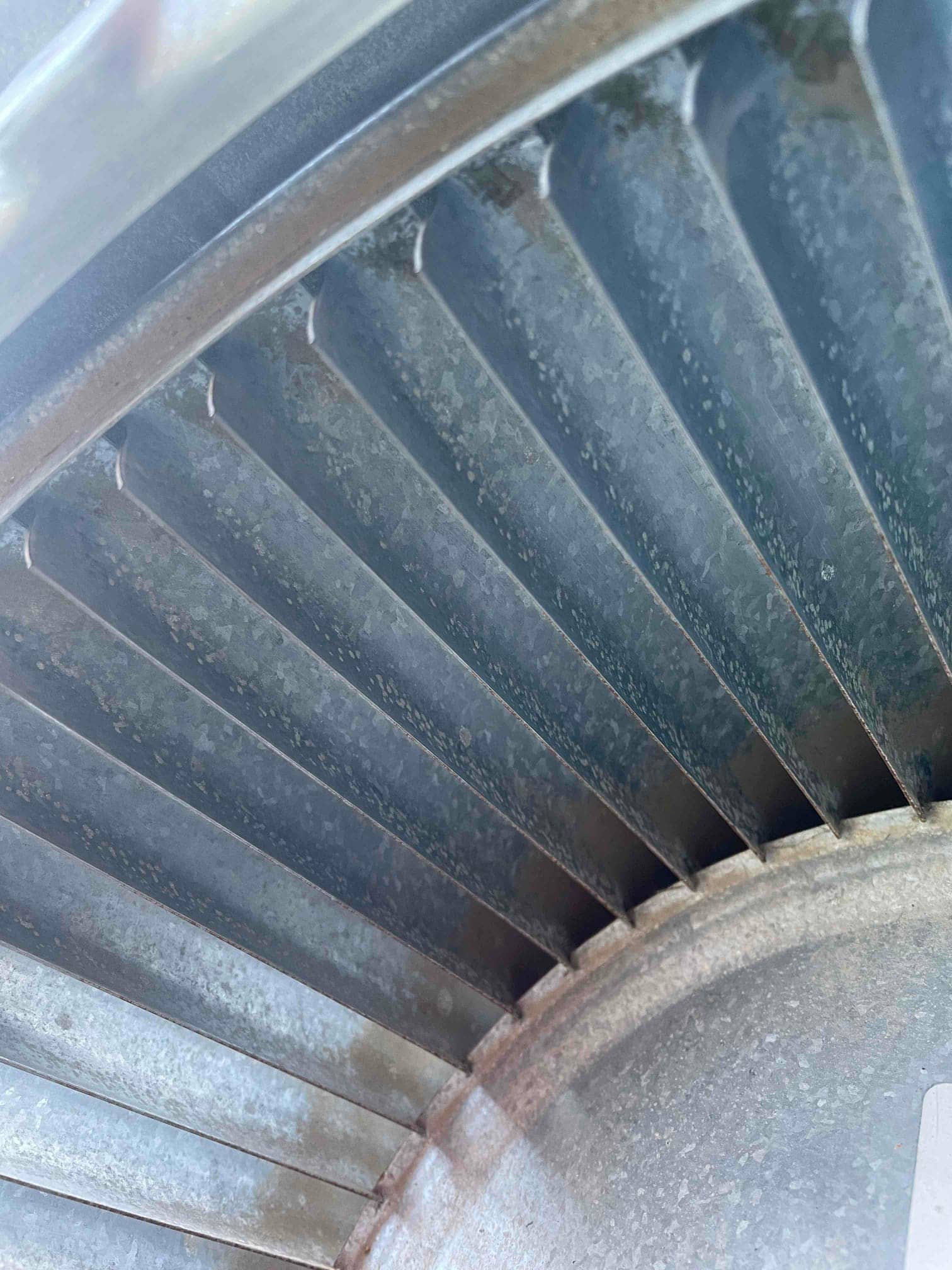 Close-up of a metal blower wheel inside the air handler, showing dust on the fins and housing.