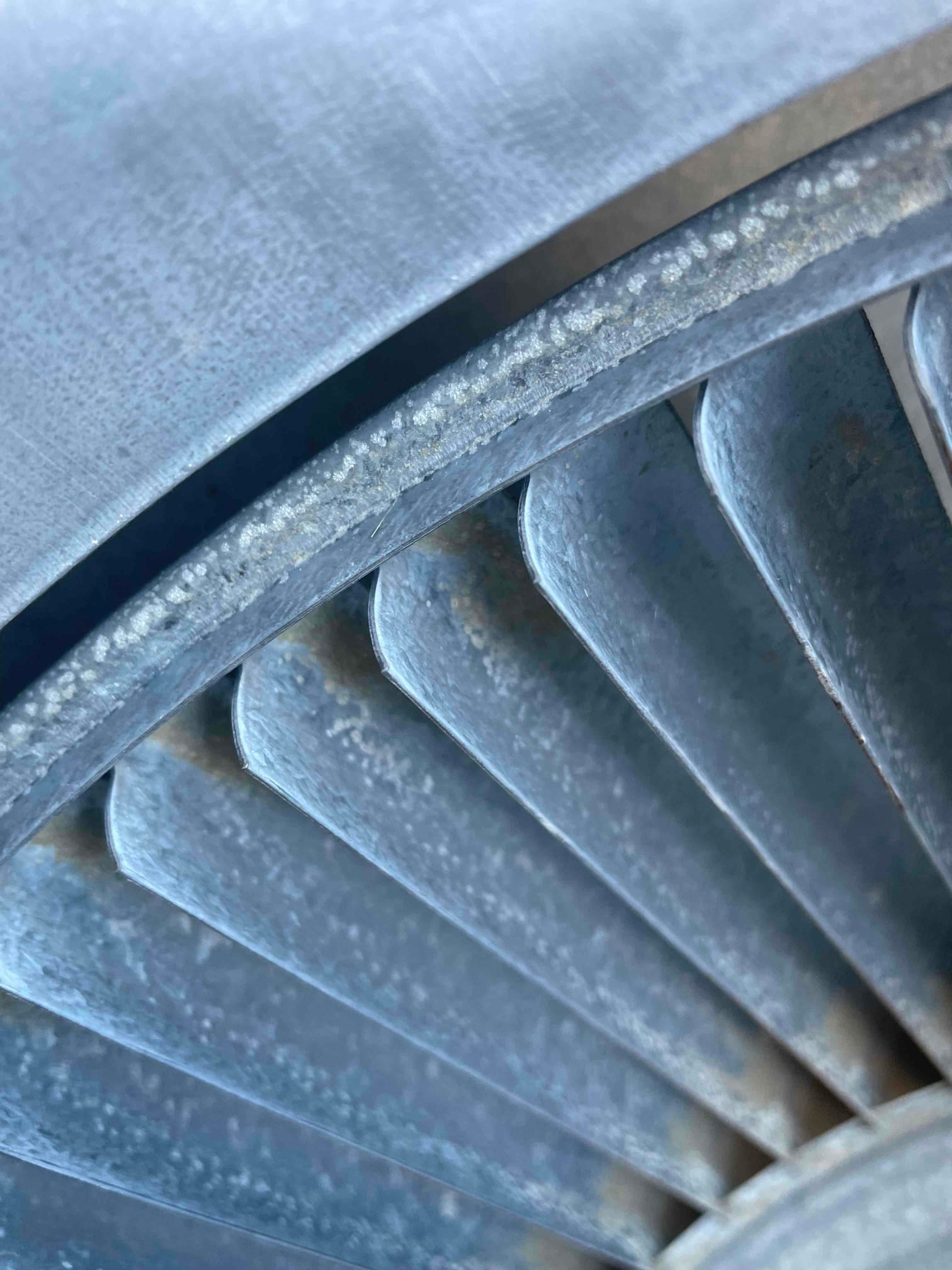 Close-up of outdoor condenser fan blades inside the shroud showing surface oxidation and accumulated debris.