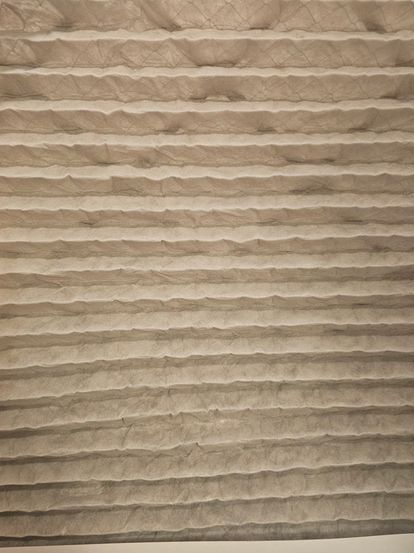 Close-up of a pleated air filter with visible dust accumulation across the folds.