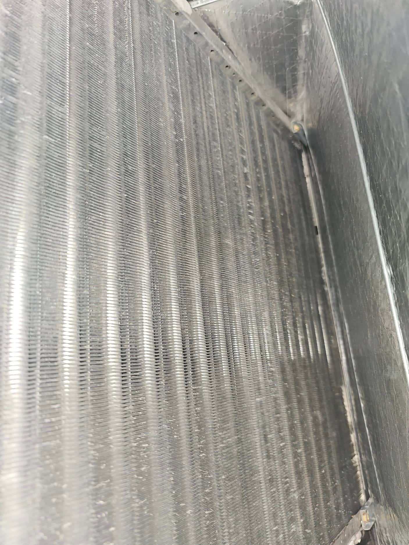 Close-up view of evaporator coil fins inside the air handler cabinet, showing aluminum fin surface and housing.