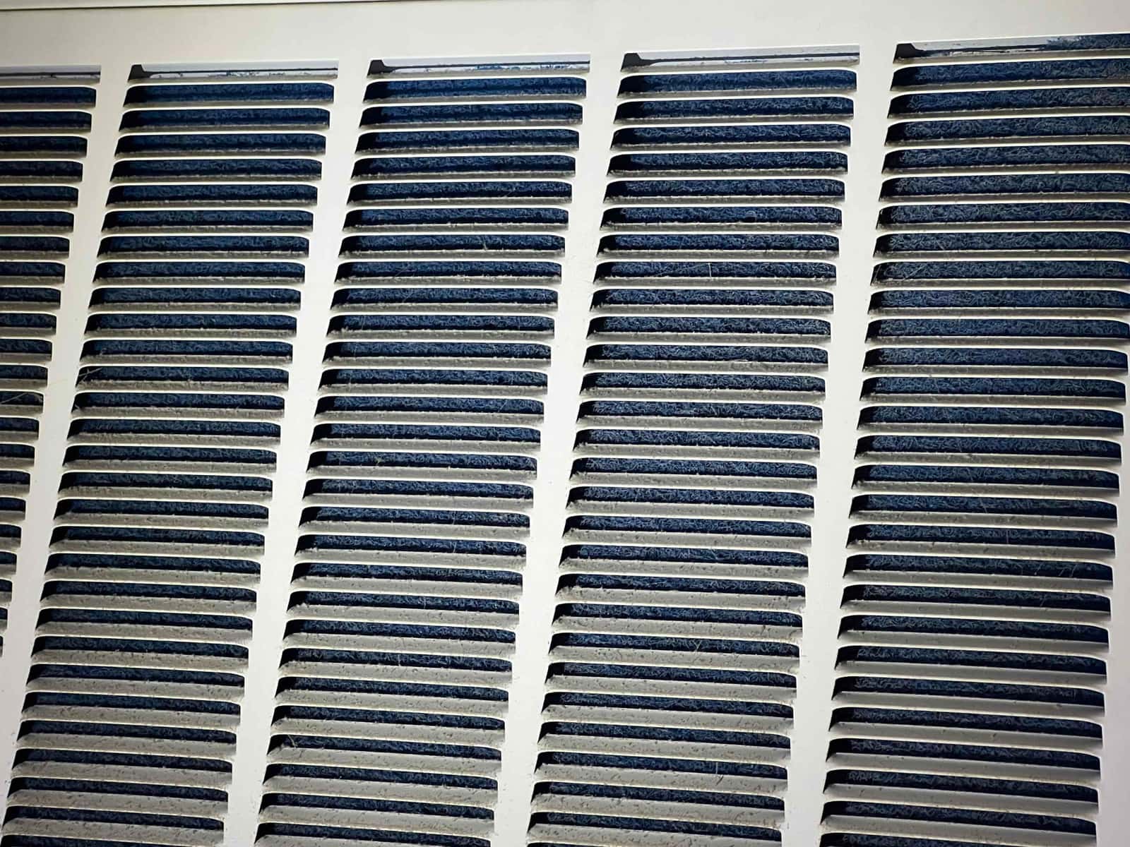Close-up of a white louvered HVAC grille with visible dust buildup along the slat edges.