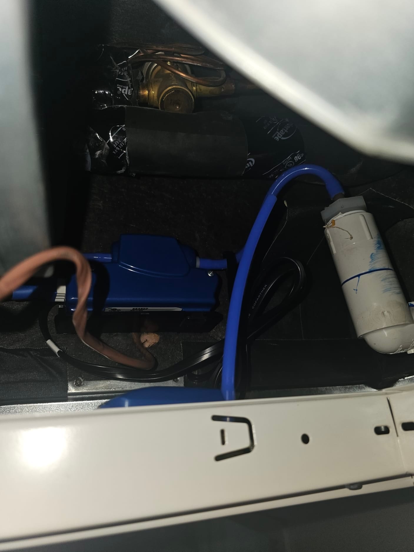 Condensate pump with blue drain tubing inside the air handler cabinet, alongside copper valve and insulated refrigerant lines.