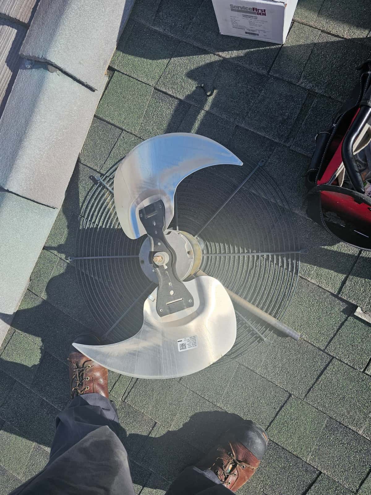 Condenser fan blade and protective grille on the roof, removed with tools and packaging visible nearby.