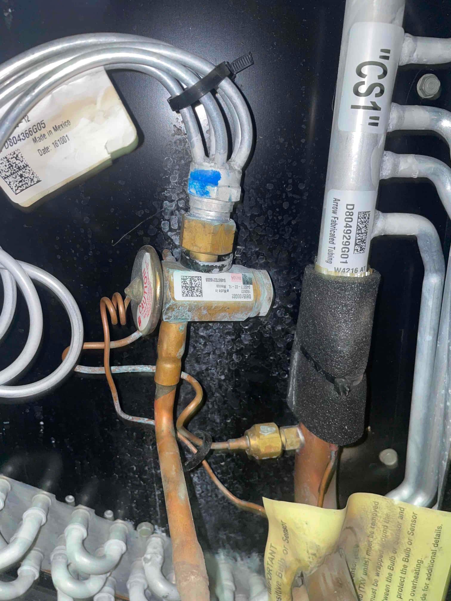 Copper refrigerant lines with a brass valve body, coiled capillary tube, and insulated suction line inside the cabinet.