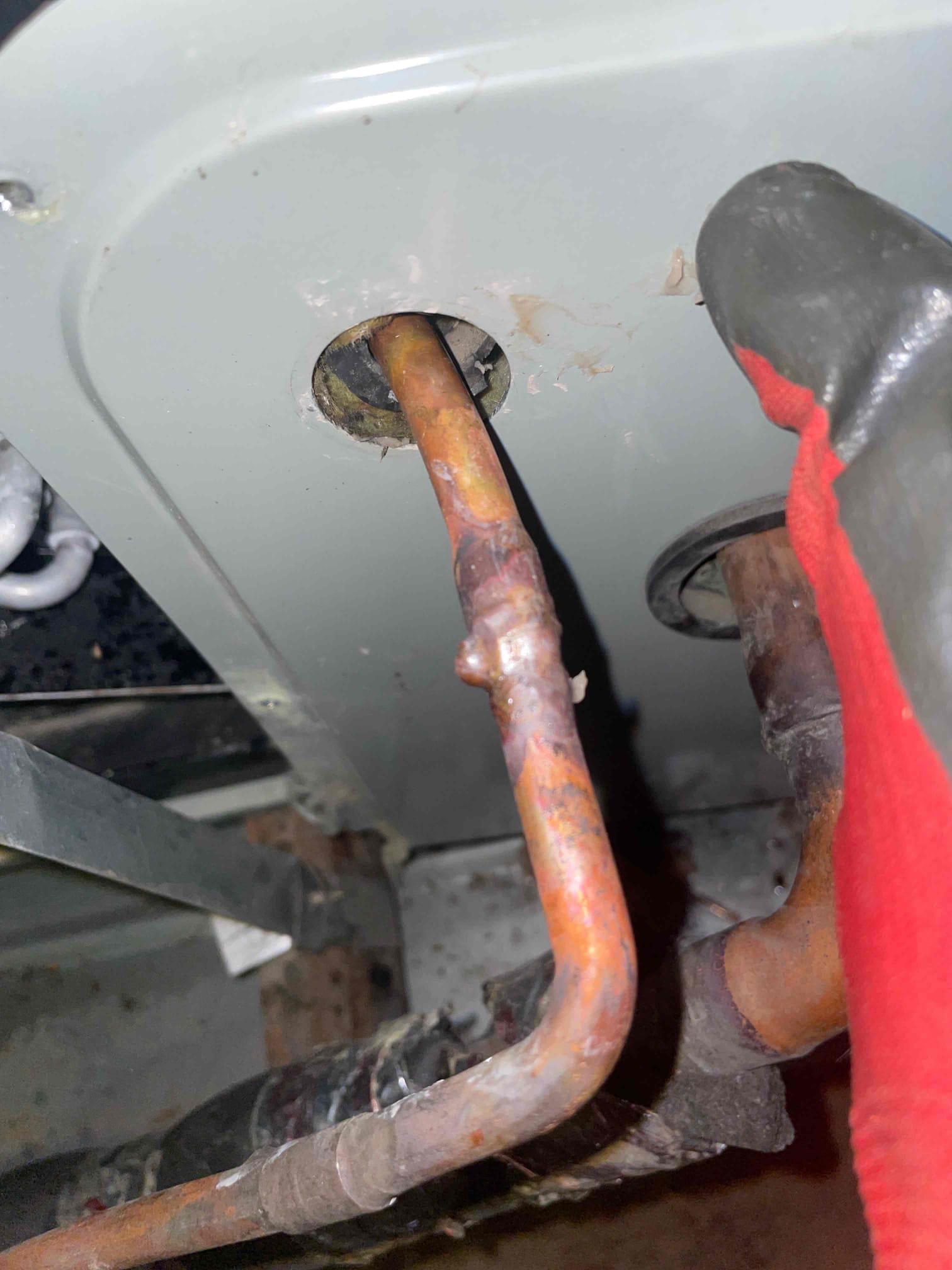 Copper refrigerant lines enter the air handler cabinet, showing brazed joints and surface oxidation near the penetration.
