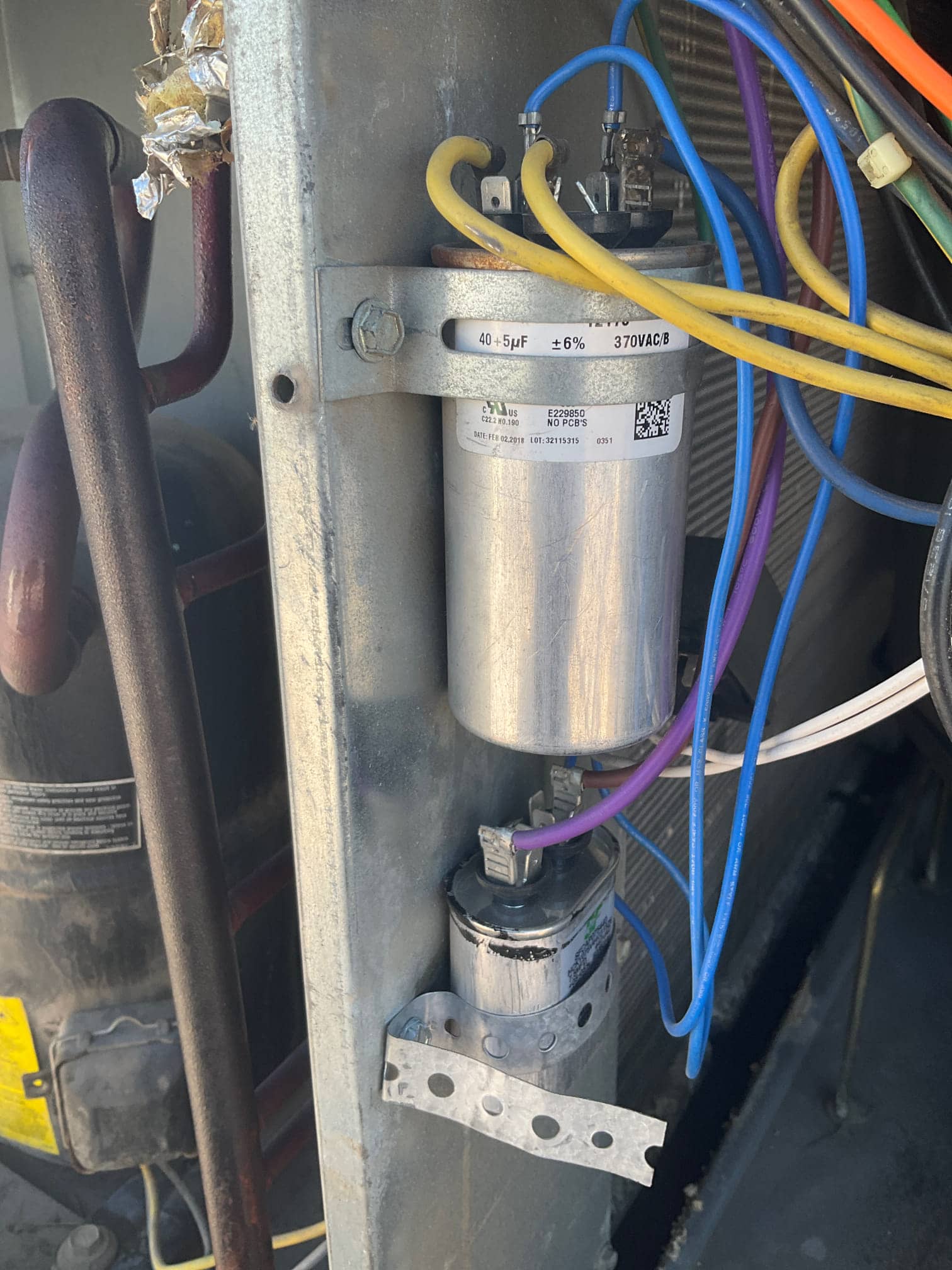 Dual-run capacitor labeled 40+5 μF ±6% 370VAC, with wiring connected to terminals, alongside a smaller capacitor mounted below.