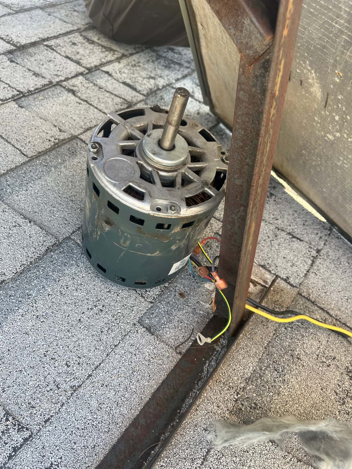 Electric motor removed and set on rooftop, with disconnected wires and a nearby rusted mounting bracket.