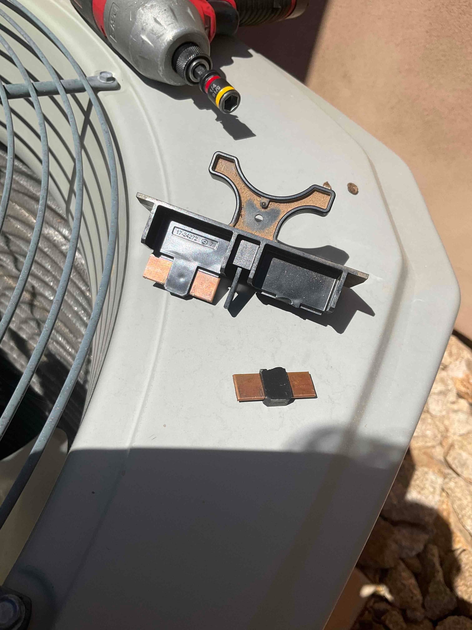 Electrical component and metal bracket placed on top of the outdoor condenser near the fan guard and power tool.