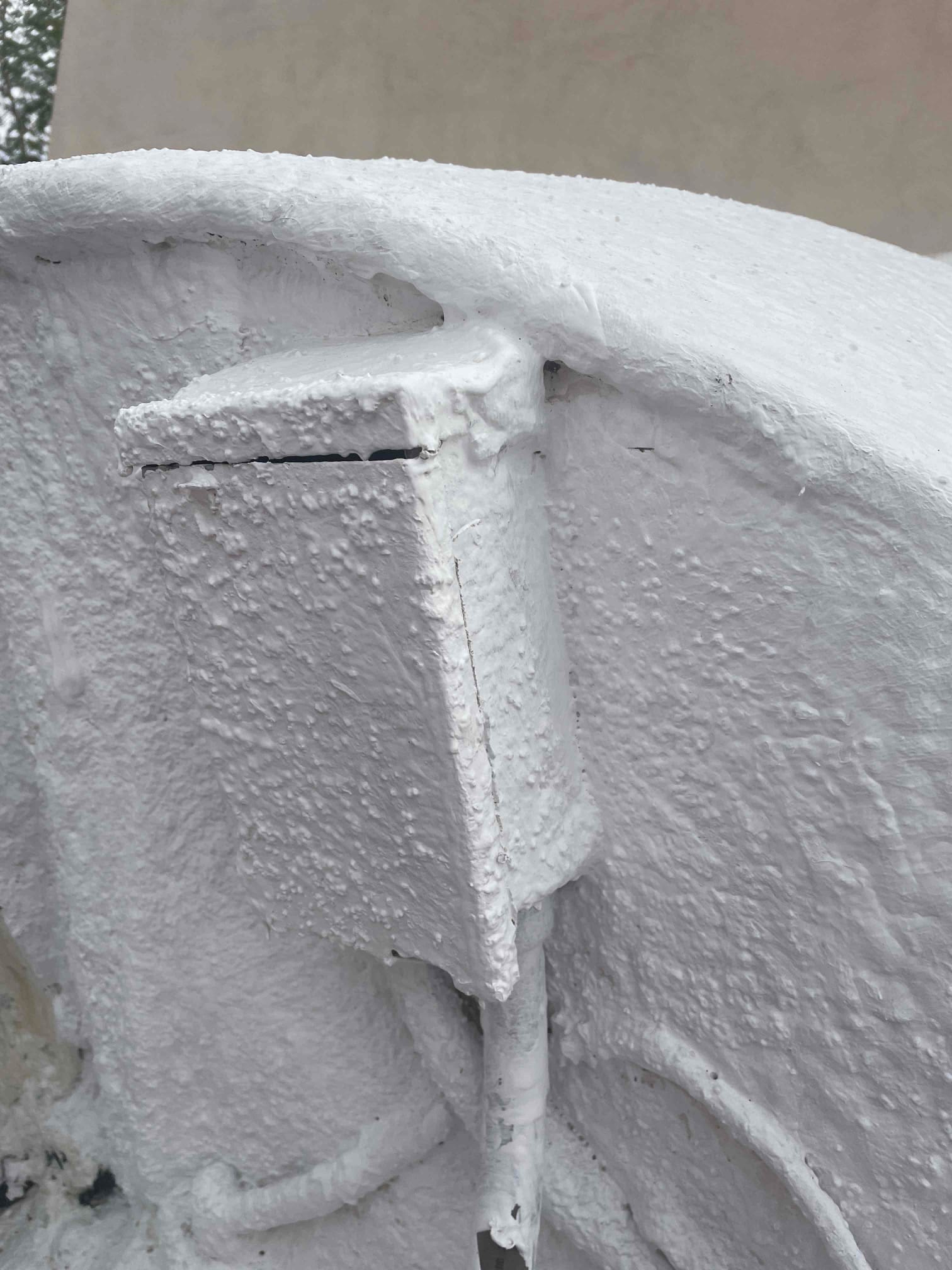 Electrical junction box and conduit on outdoor HVAC equipment, fully covered in thick white coating and overspray.