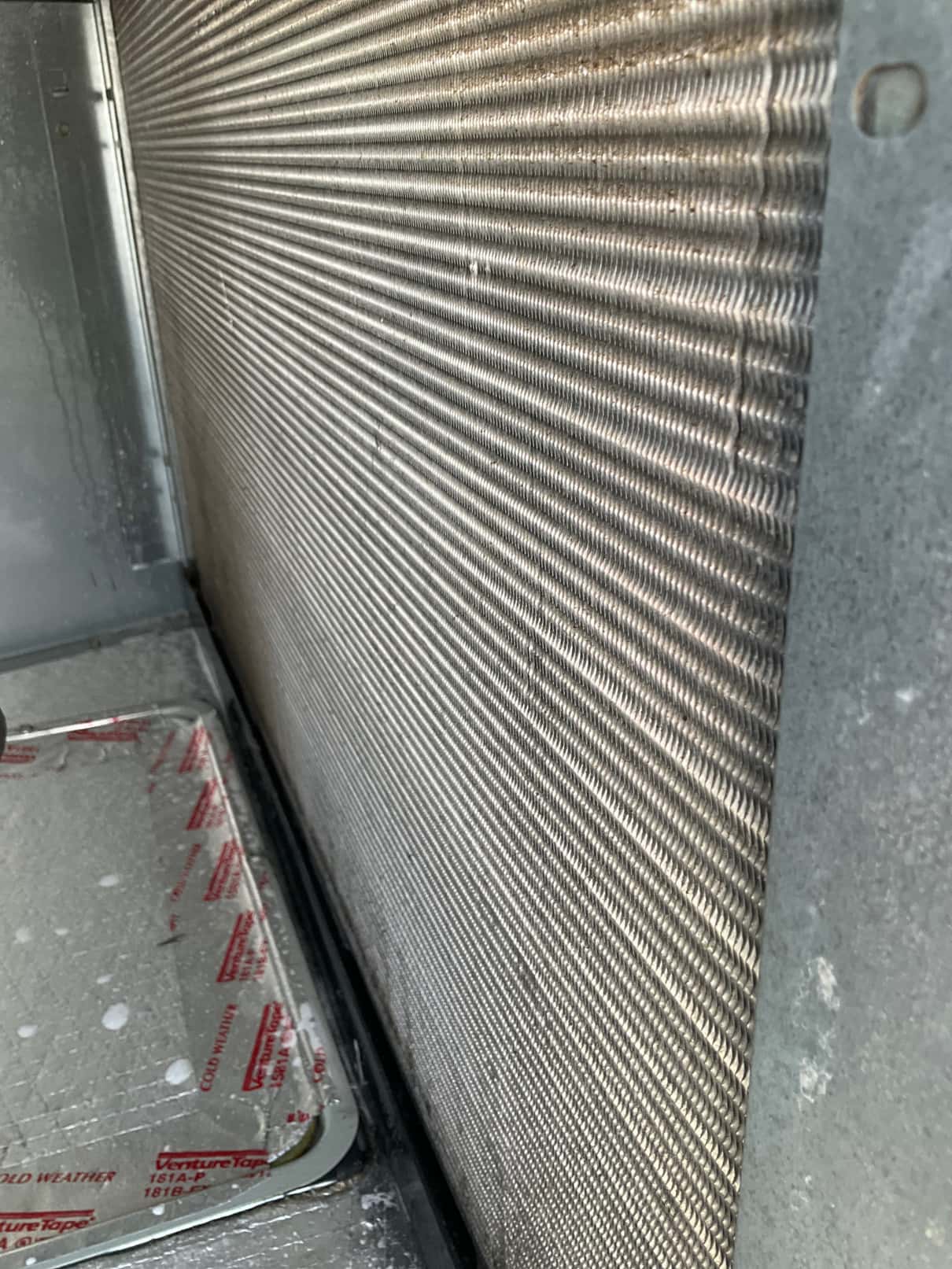 Evaporator coil fin surface inside the air handler cabinet, with drain pan and foil tape visible below.