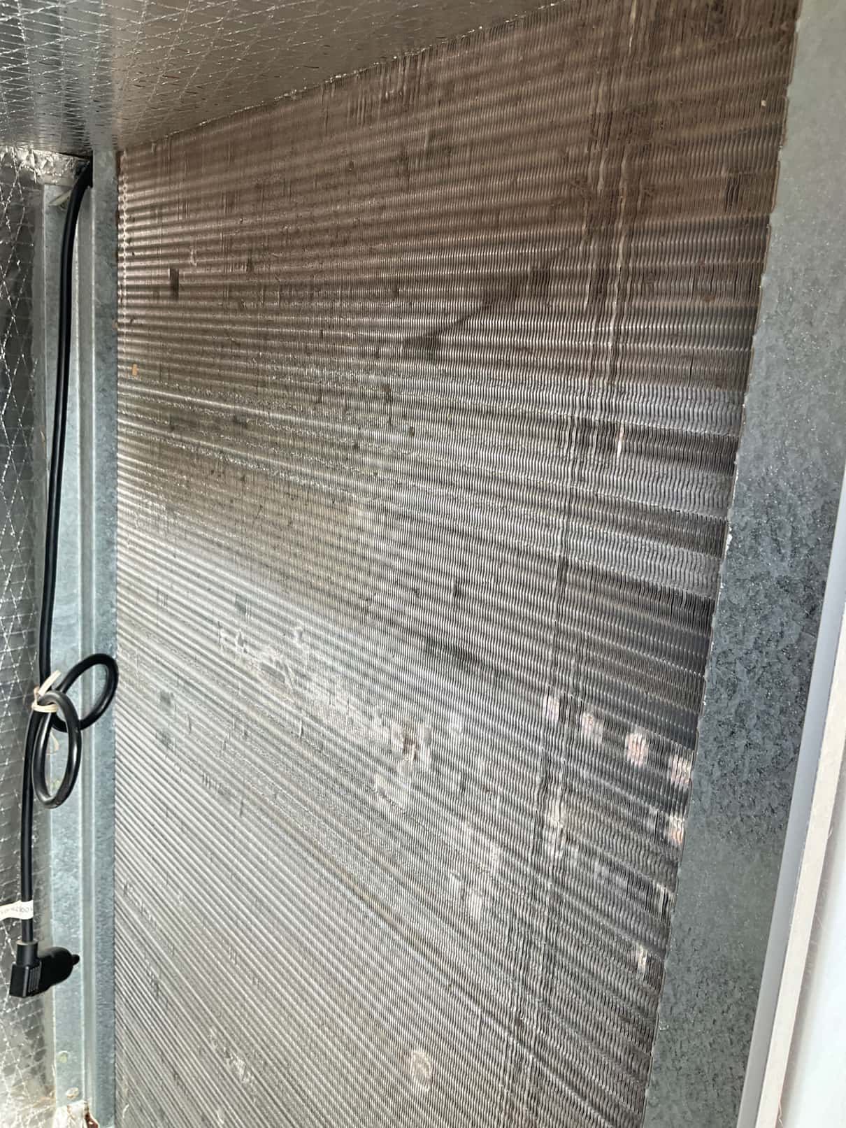 Evaporator coil fins inside the air handler cabinet, showing surface smudges and scattered bent fins across the face.