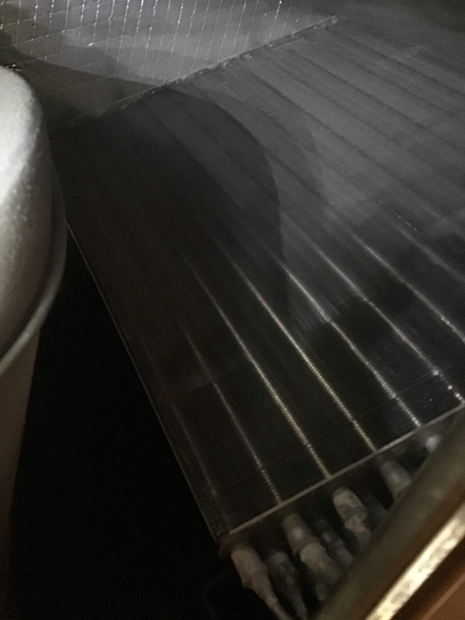 Evaporator coil fins and refrigerant distributor tubes inside the air handler compartment under flashlight.