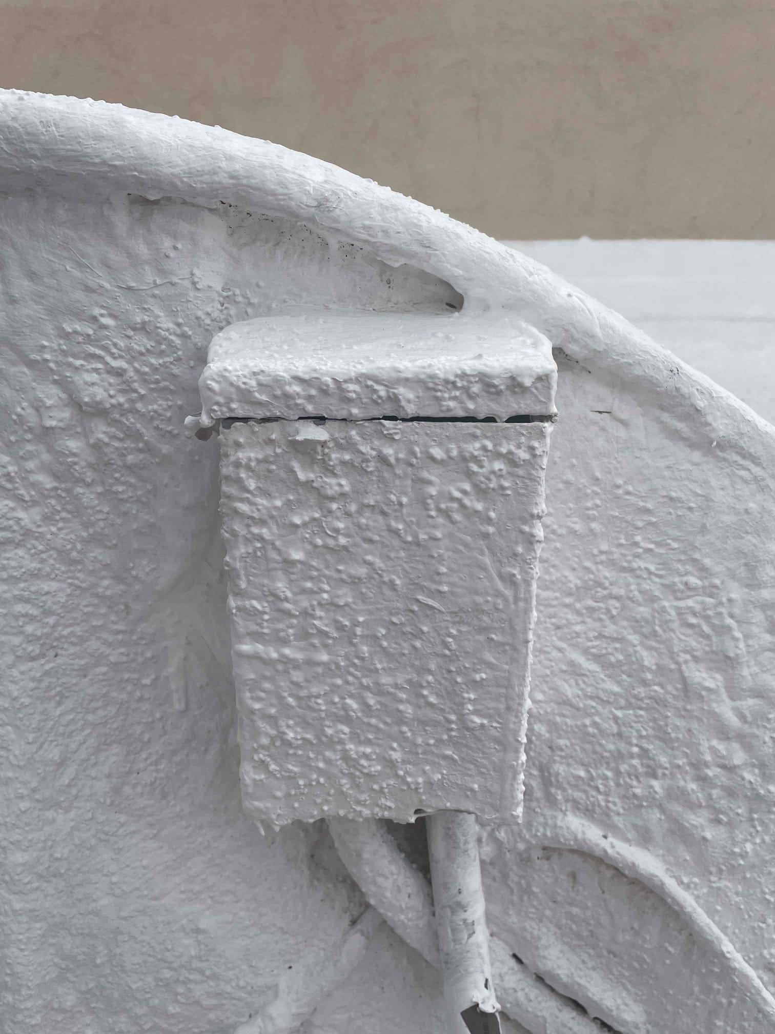Exterior electrical box with conduit is heavily coated in white paint and textured coating.