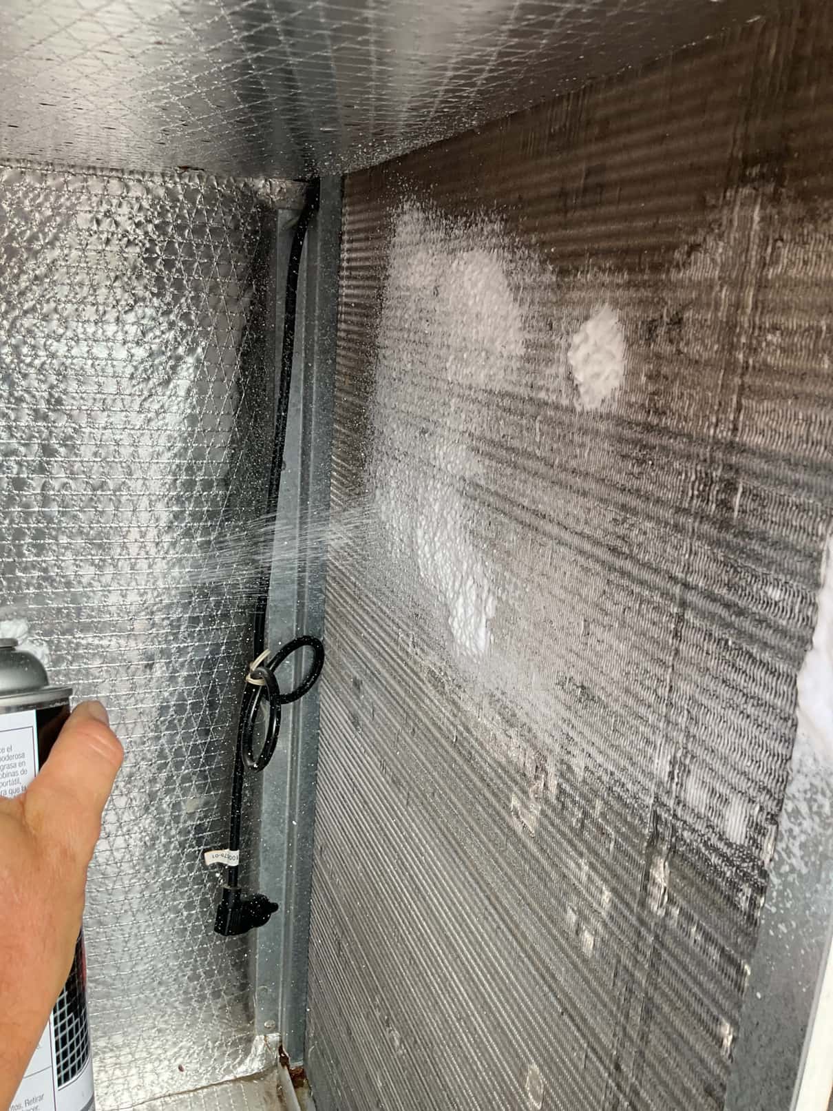 Foaming coil cleaner is being sprayed onto the evaporator coil inside the air handler cabinet.