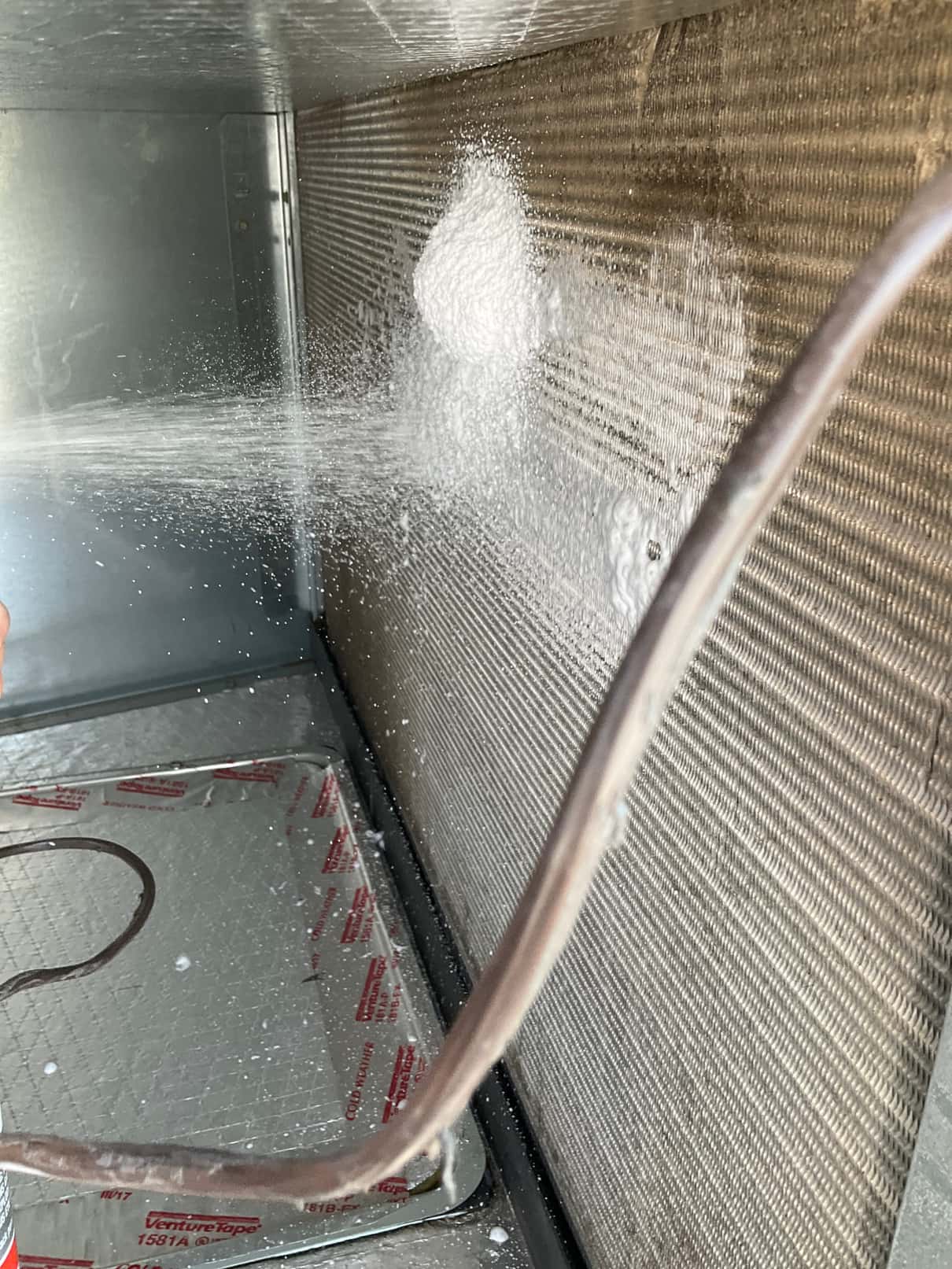 Foaming coil cleaner sprays onto the indoor evaporator coil surface and drain pan inside the air handler.
