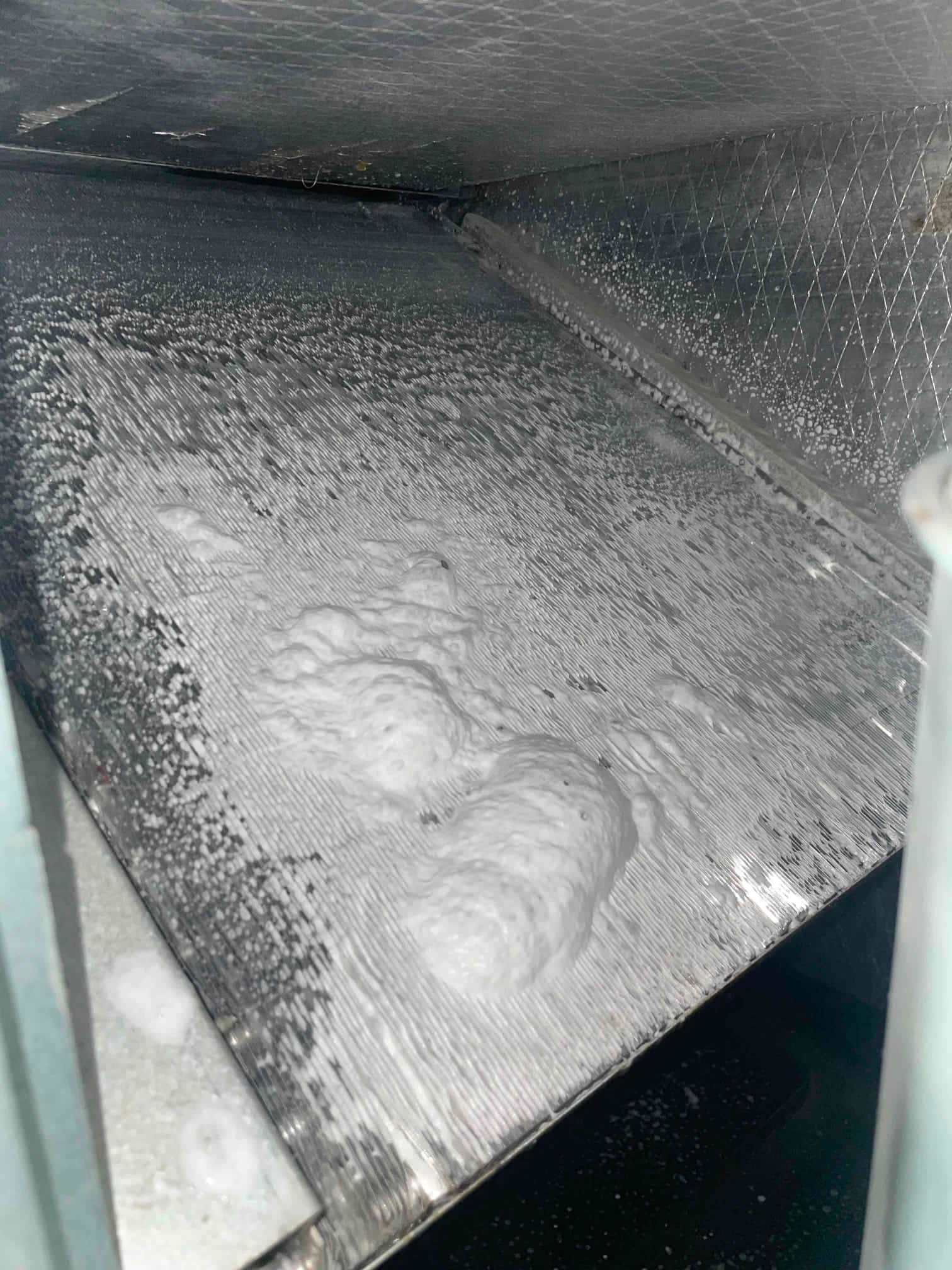 Foil-lined metal panel with foamy bubbles and small droplets across the surface inside an HVAC enclosure.