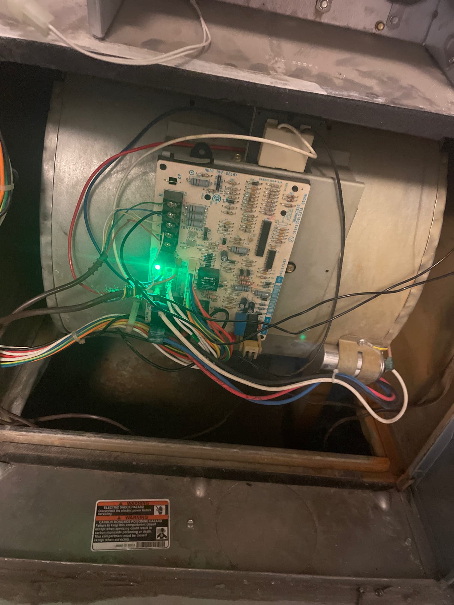 Furnace control board mounted on blower housing with green status LED illuminated and connected wiring harnesses.