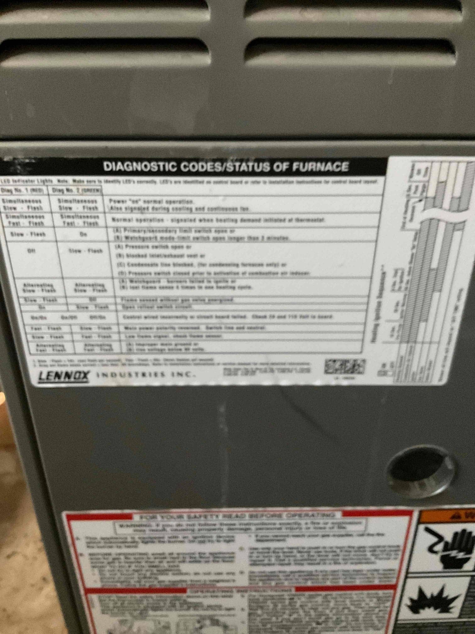 Furnace front panel with diagnostic codes and safety instruction labels visible near an open knockout port.