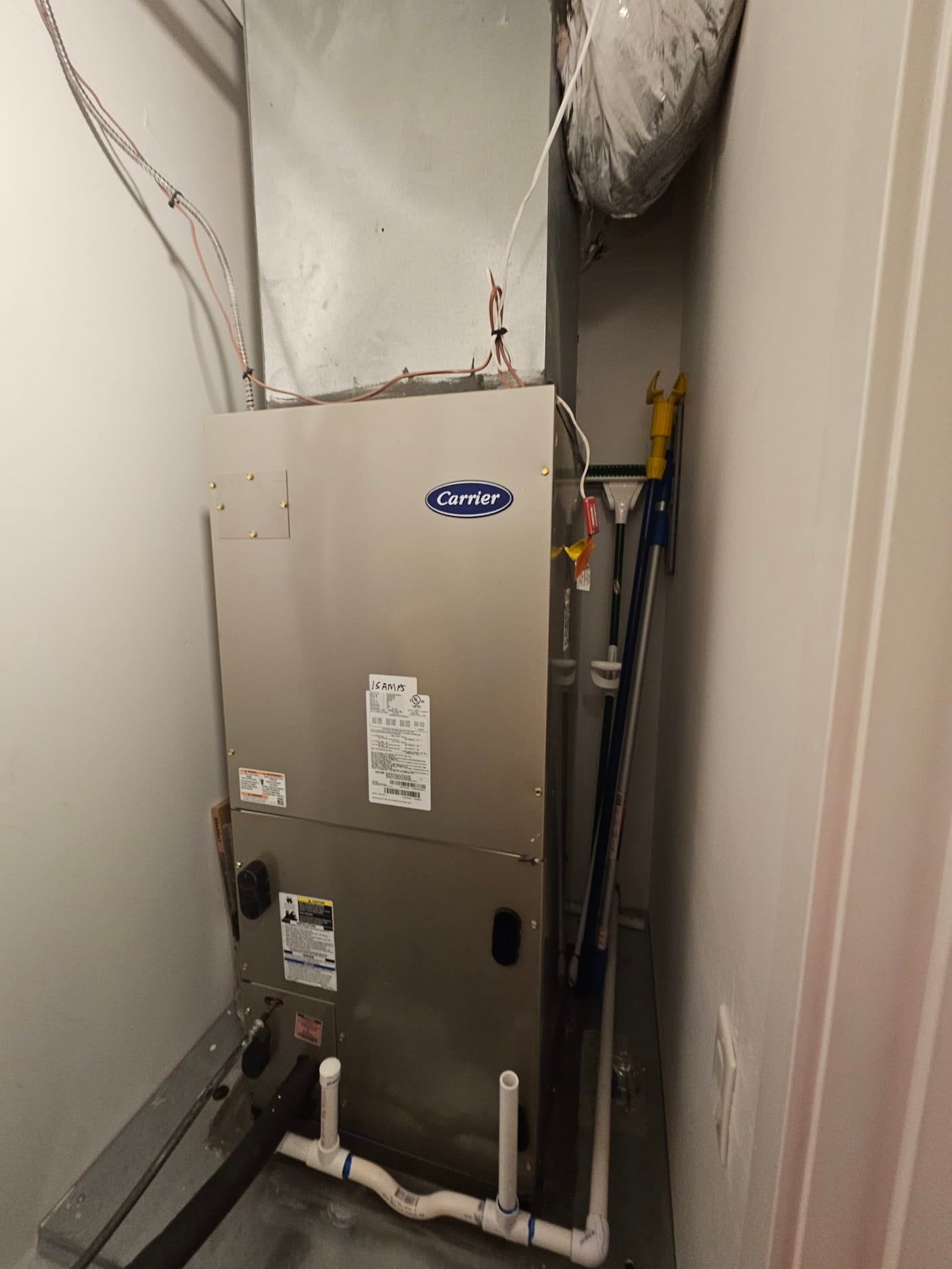 Indoor air handler in a closet with duct connection, condensate drain piping, insulated refrigerant line, and wiring at the top.