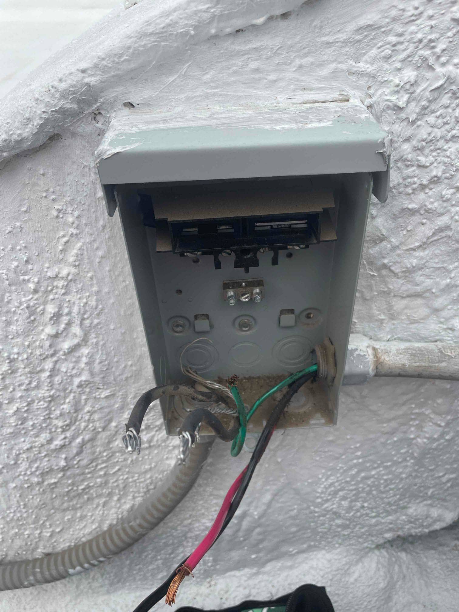 Open electrical disconnect enclosure on exterior wall showing loose black, red, and green wires with exposed copper conductors.