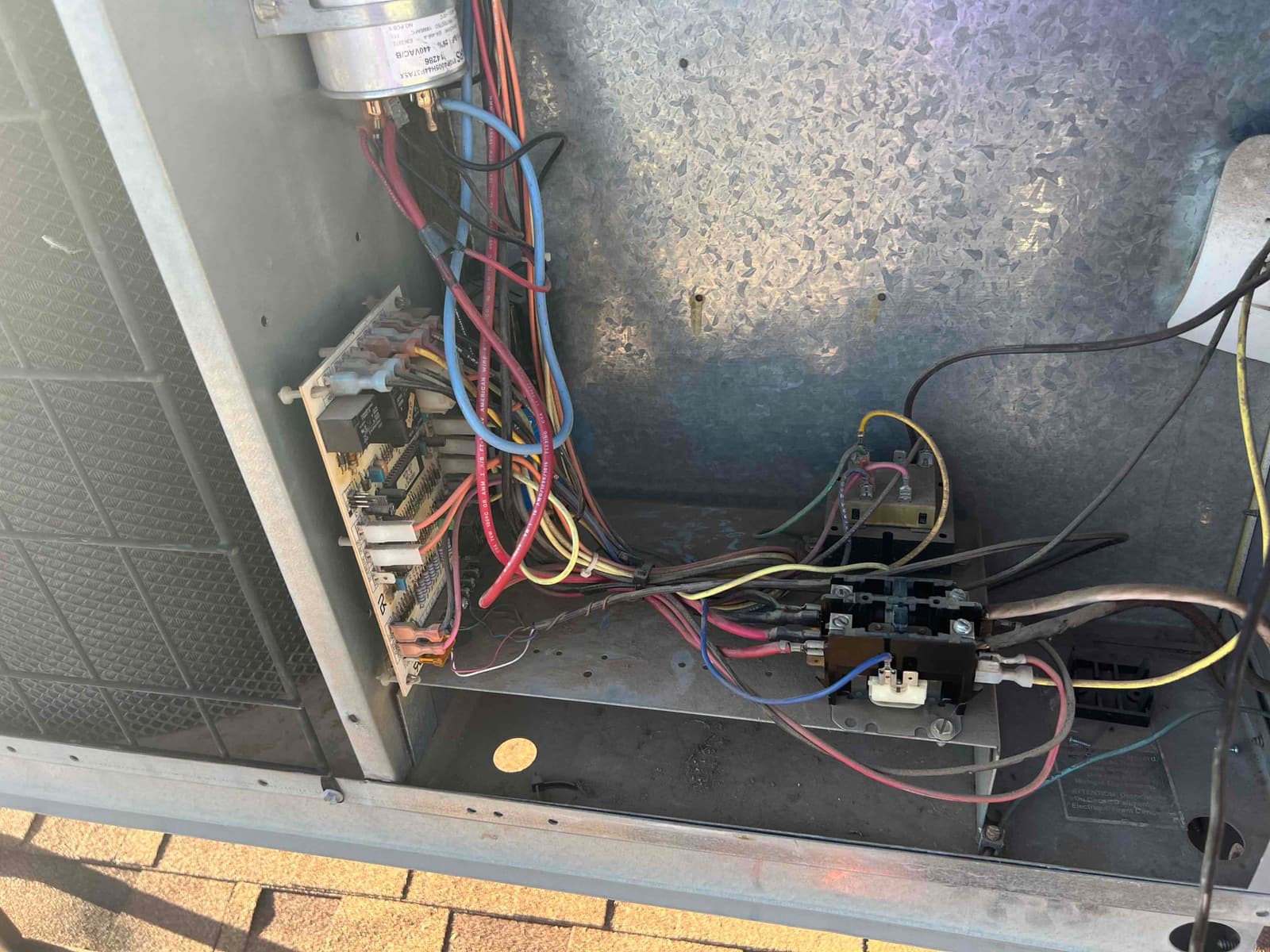 Open outdoor unit electrical compartment showing control board, multiple colored wiring harnesses, and a contactor mounted on the metal base.