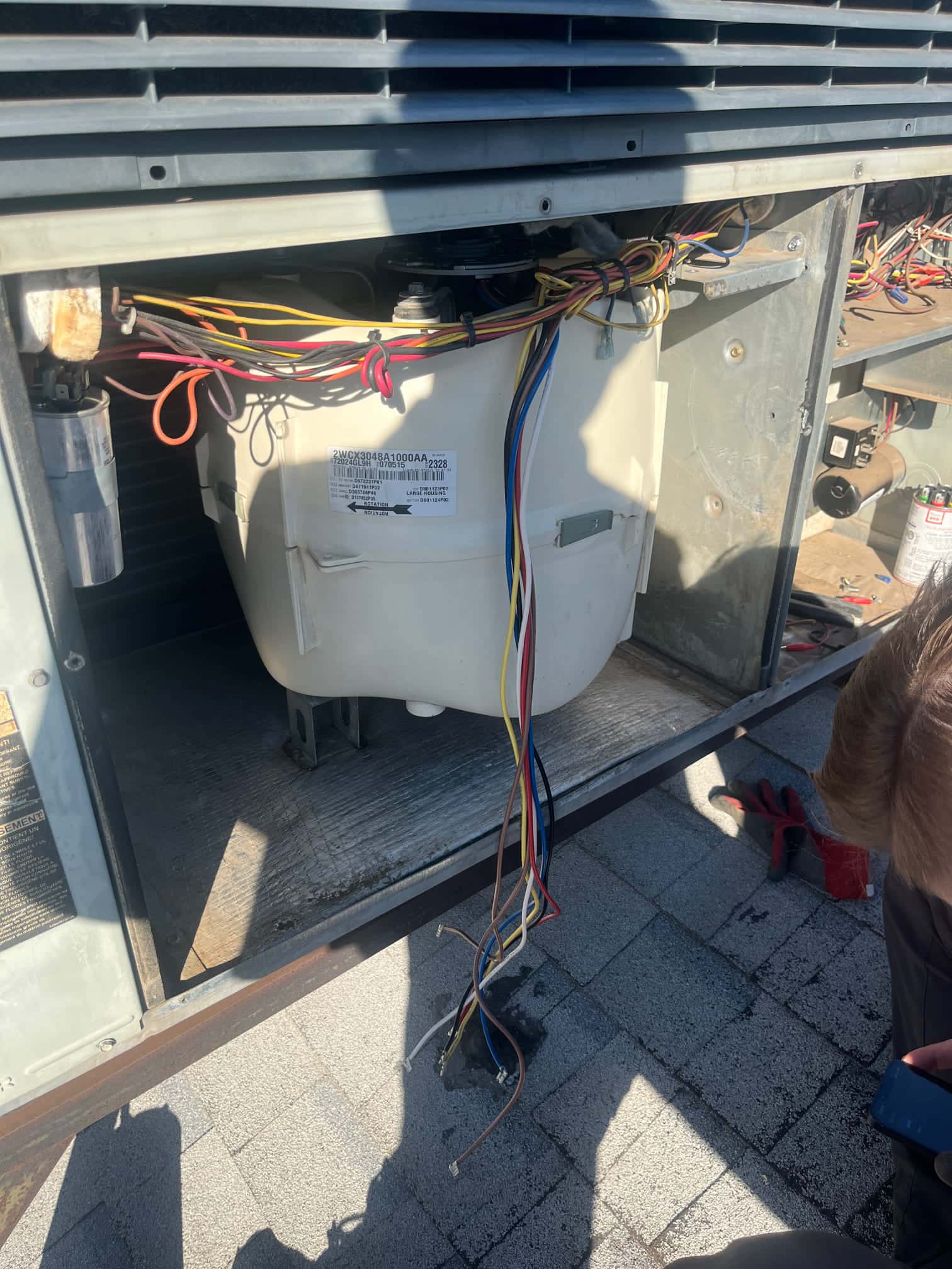 Open rooftop unit compartment shows blower housing and motor with bundled wiring, a mounted capacitor, and several disconnected wires hanging below.