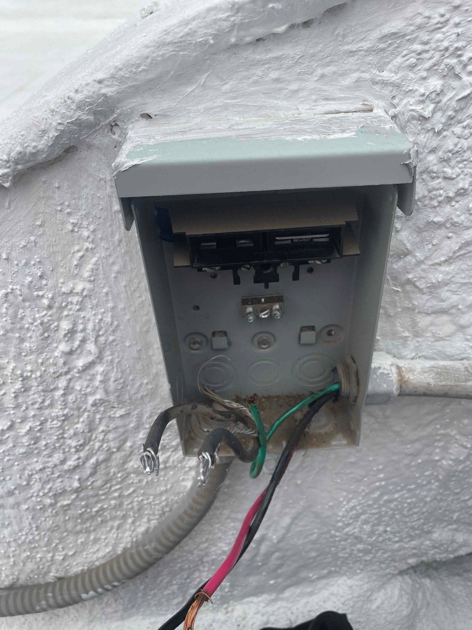 Outdoor AC disconnect box open, showing cut and stripped wires, green ground, and conduit entering the enclosure.