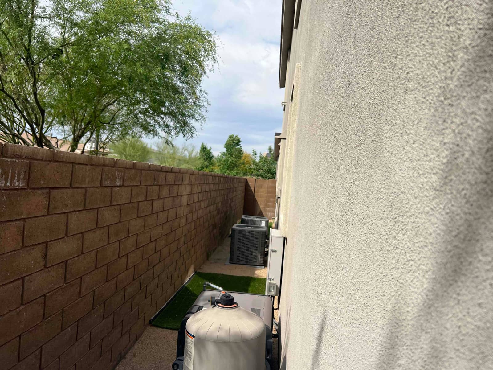 Two outdoor air-conditioning condenser units positioned along the house exterior wall, with wall-mounted service boxes above.