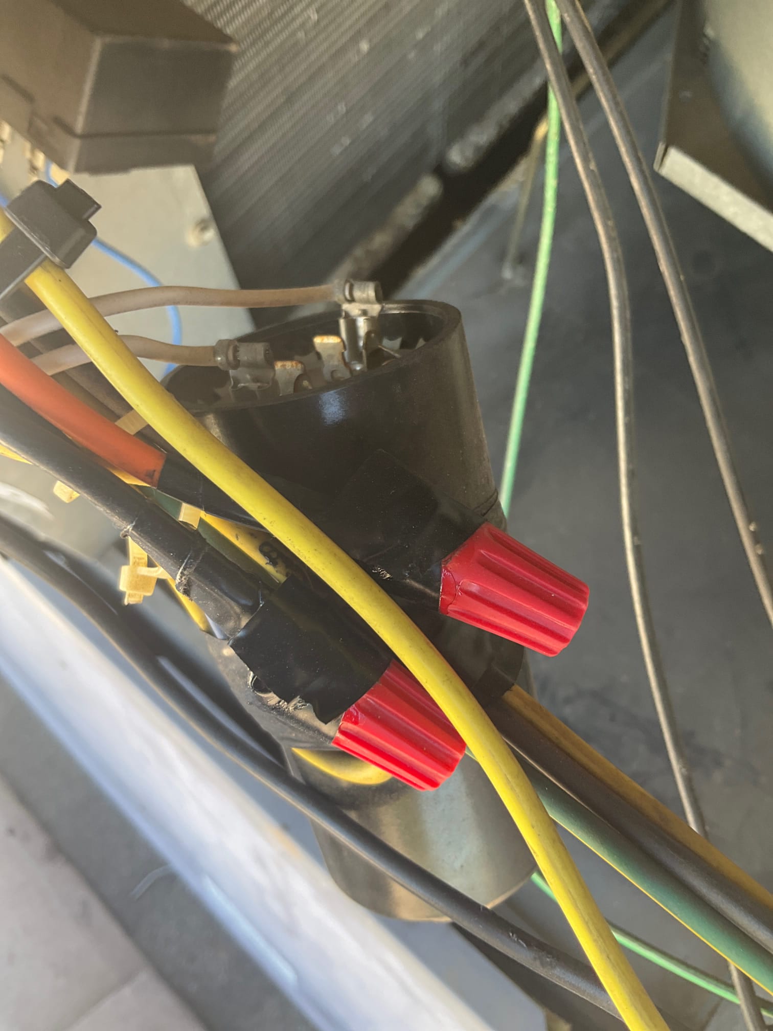 Outdoor condenser electrical wiring with red wire nuts and taped splices near component terminals inside the unit.