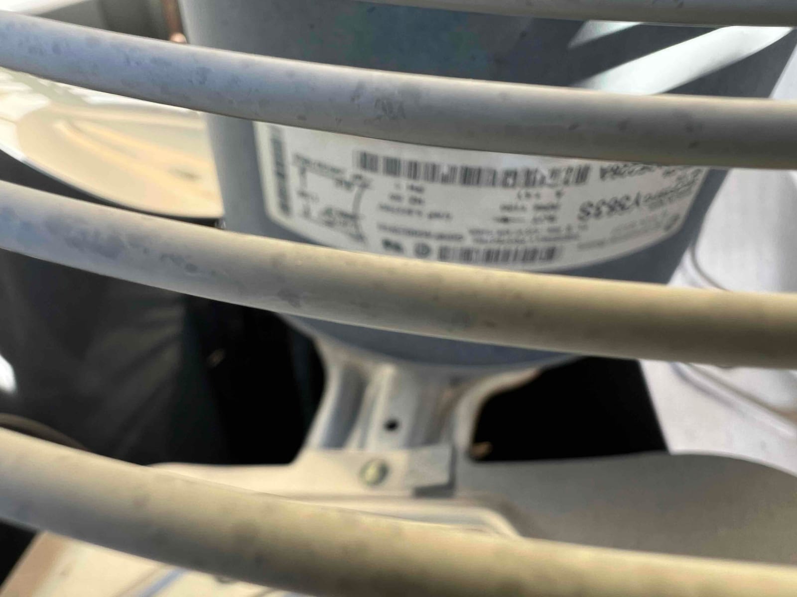 Outdoor condenser fan motor under the protective grille, with mounting hub and unreadable specification label visible.