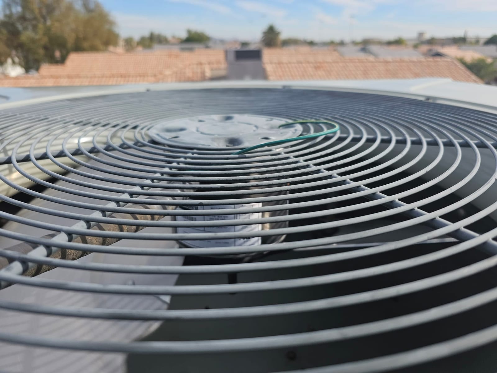 Outdoor condenser top grille showing fan motor hub, green ground wire, and cylindrical run capacitor inside cabinet.