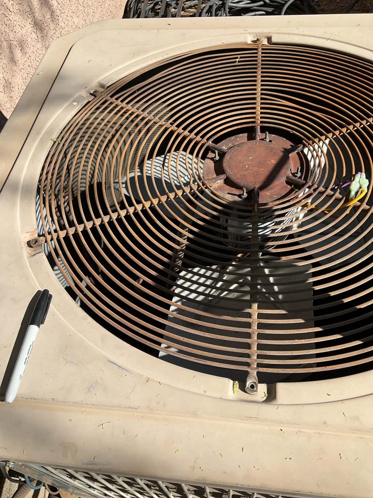 Outdoor condenser top shows rusted fan guard and central hub, with dirt and small debris present.